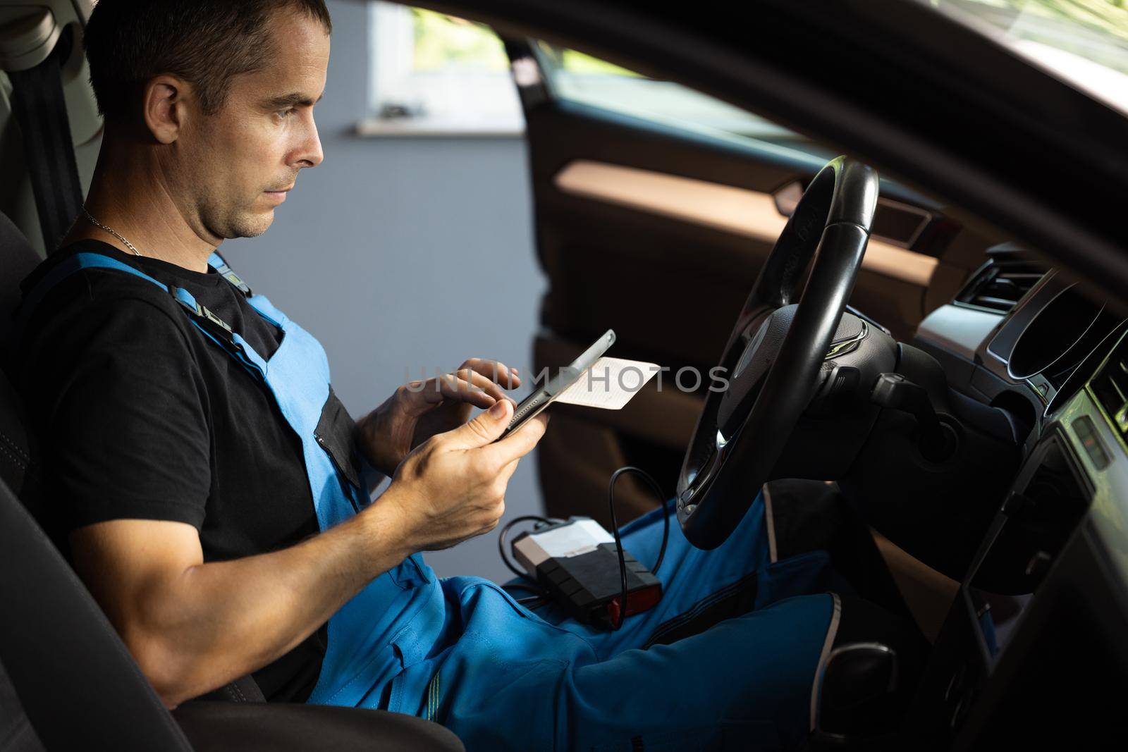 Automotive mechanic running diagnostics software on tablet computer. Mechanic sitting in car and working on laptop while doing vehicle diagnostic test in auto service garage.