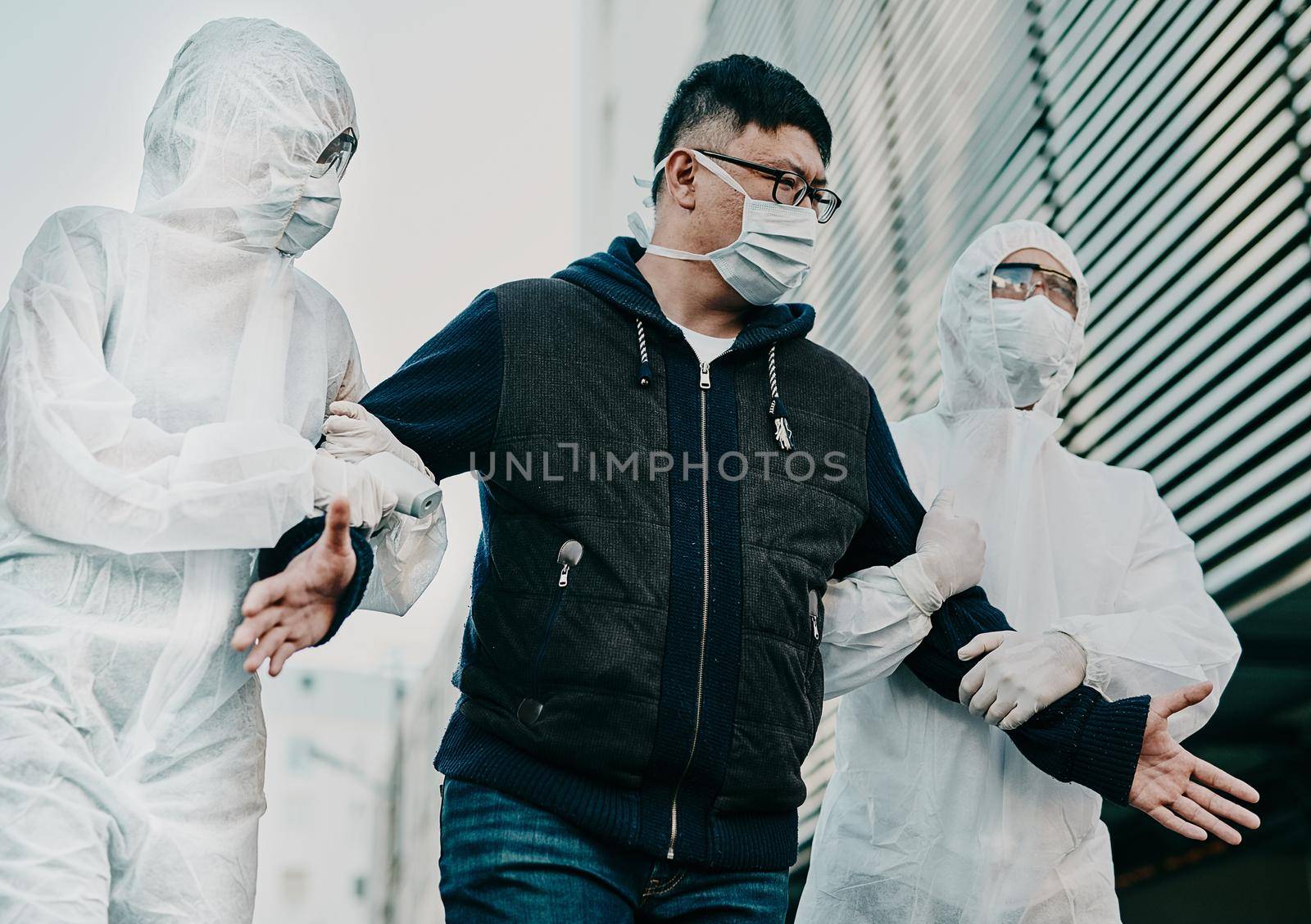 Man breaking covid regulation getting taken away or arrested by healthcare workers wearing hazmat protective suits. Male removed for not following the rules or restrictions of coronavirus pandemic. by YuriArcurs
