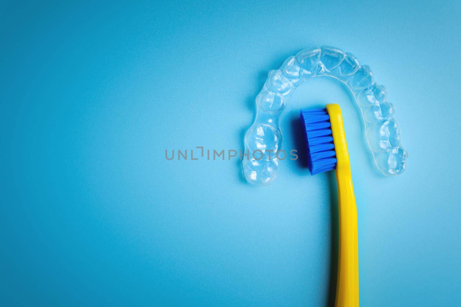 An invisible plastic aligner for correcting teeth to straighten teeth lies on a blue background with a toothbrush.