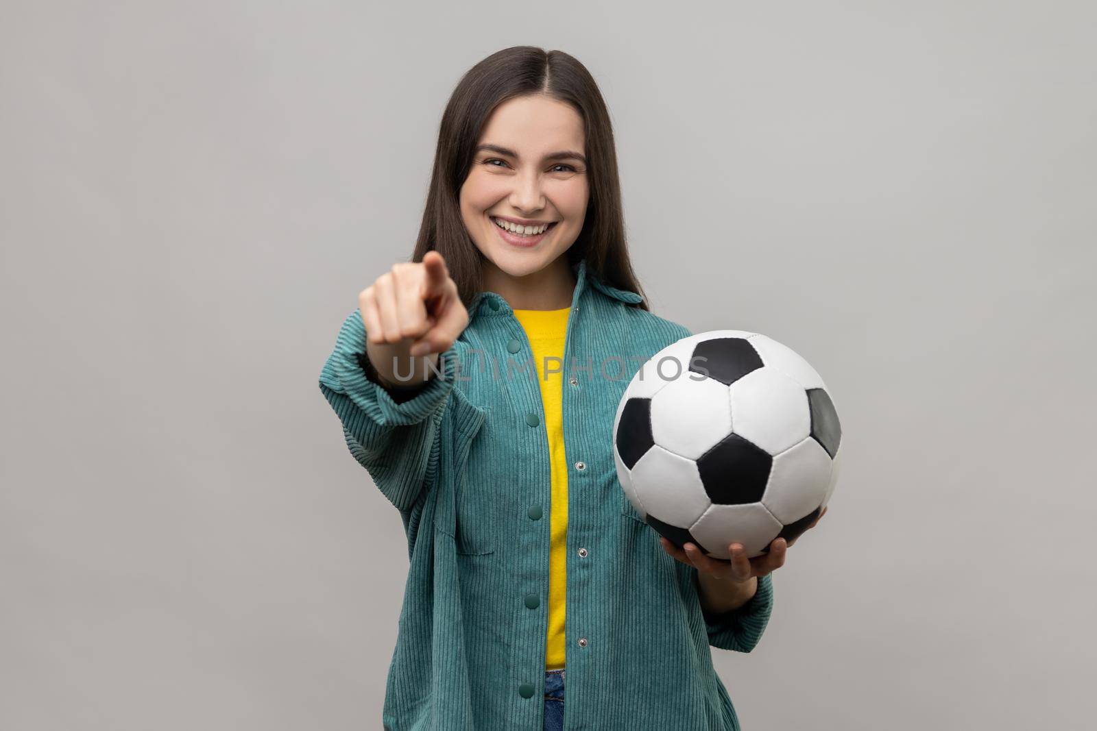 Beautiful woman holding soccer ball, looking at camera with toothy smile, pointing finger to camera. by Khosro1