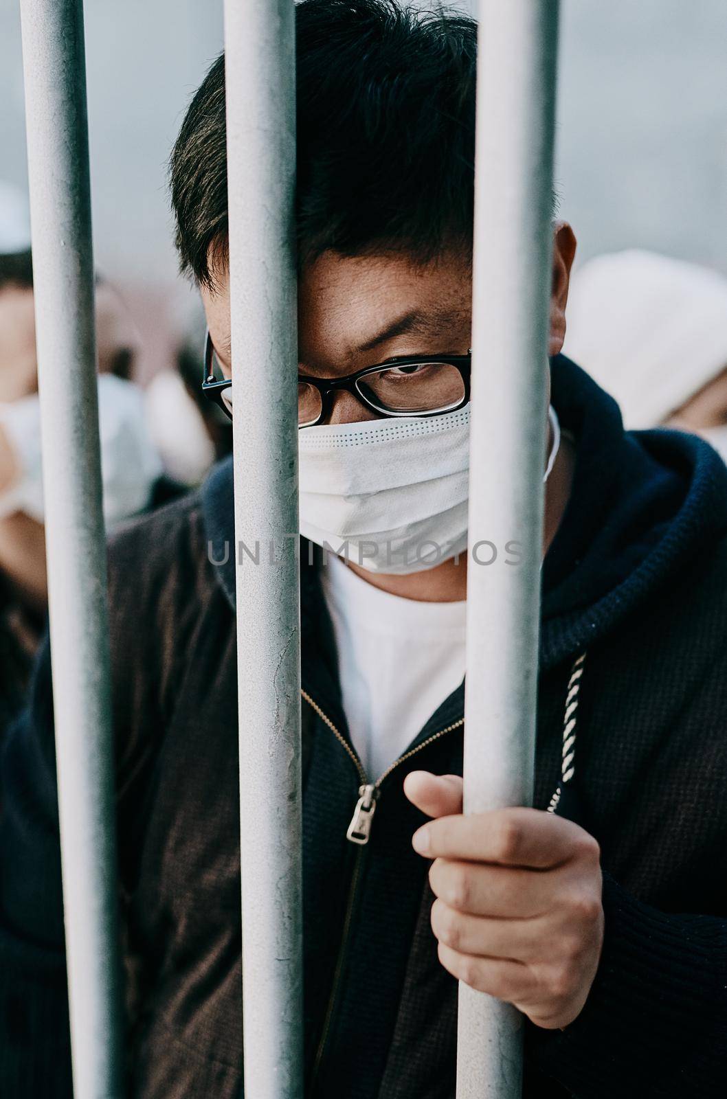 Lockdown, isolation and covid travel ban with a man in a mask behind bars during an international pandemic. Corona virus restrictions, feeling like a prisoner or captive during a global shutdown.