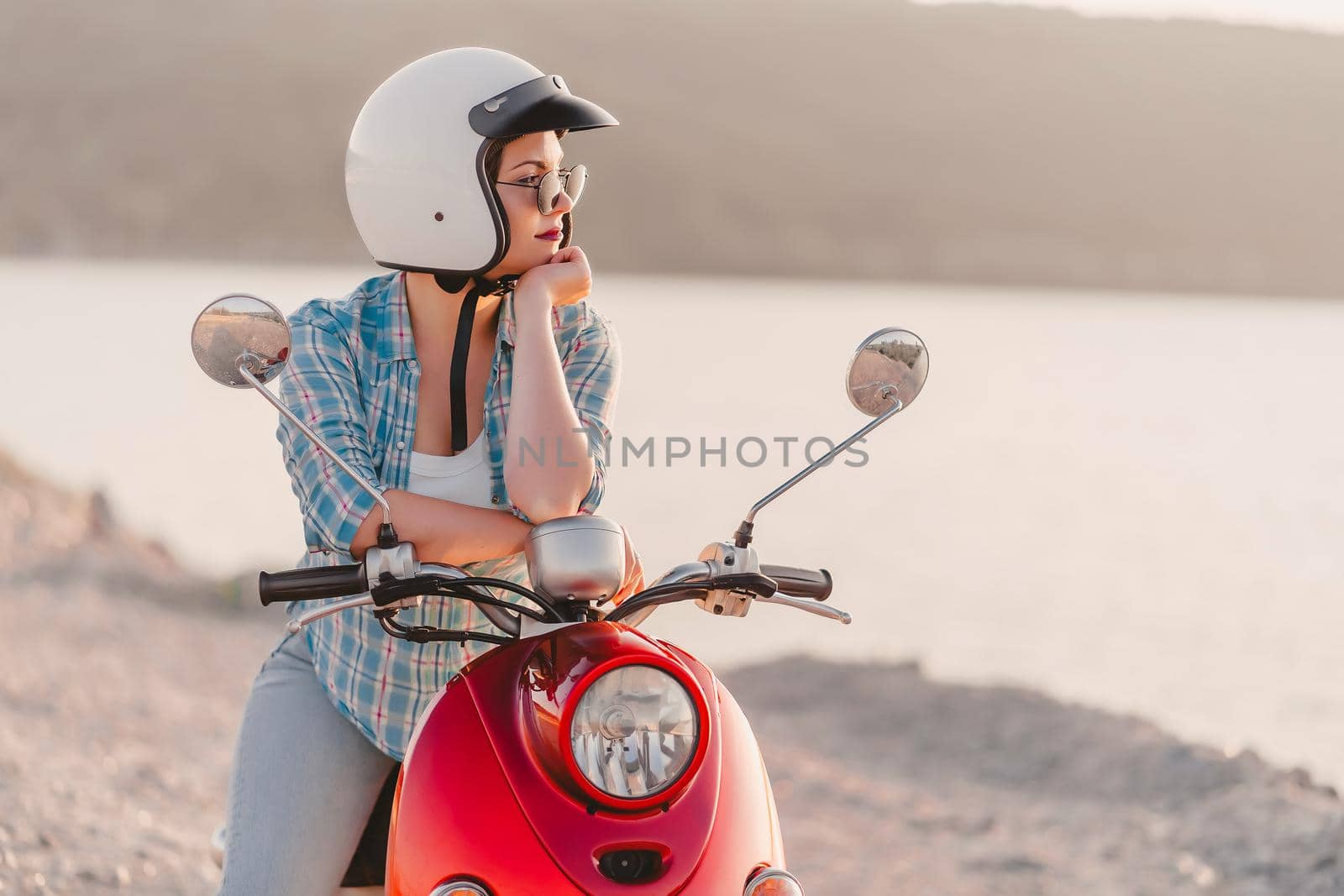 Young pretty woman's portrait. Girl in white helmet and eyeglasses sitting on red retro scooter at nature background. High quality photo