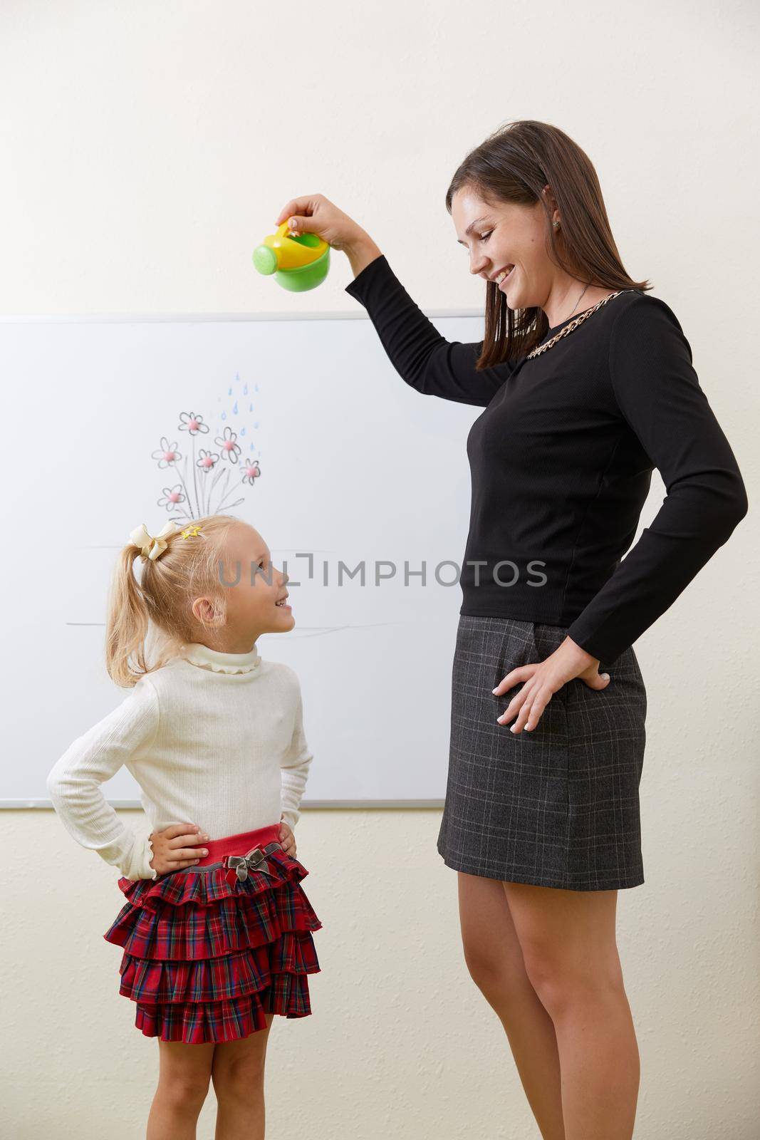 Teacher watering flower drawing on a white board with little girl standing near board by Mariakray