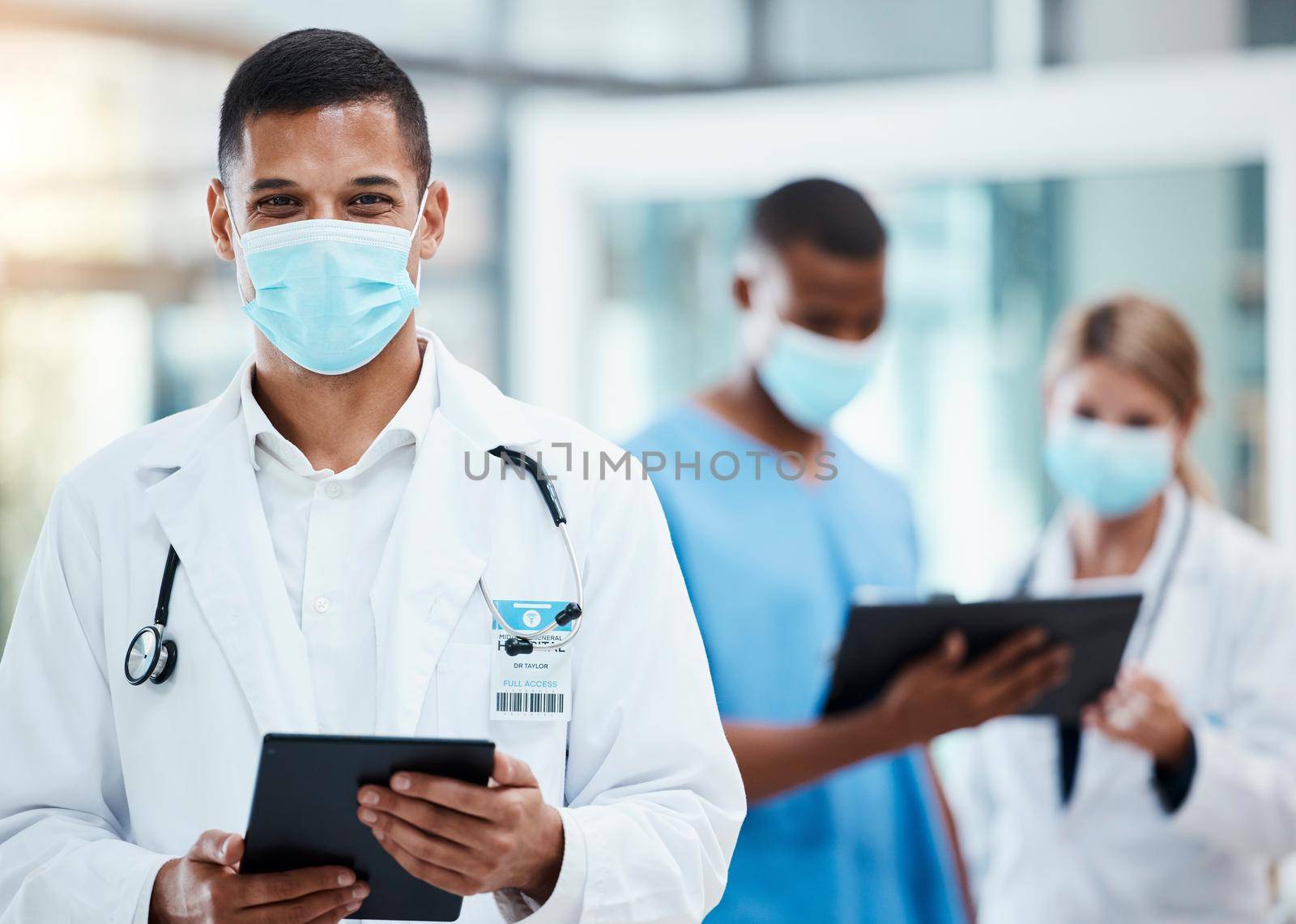 A successful male doctor browsing the internet, using a tablet and wearing a mask inside a hospital. Portrait of a healthcare professional searching covid, flu or disease on a digital device.