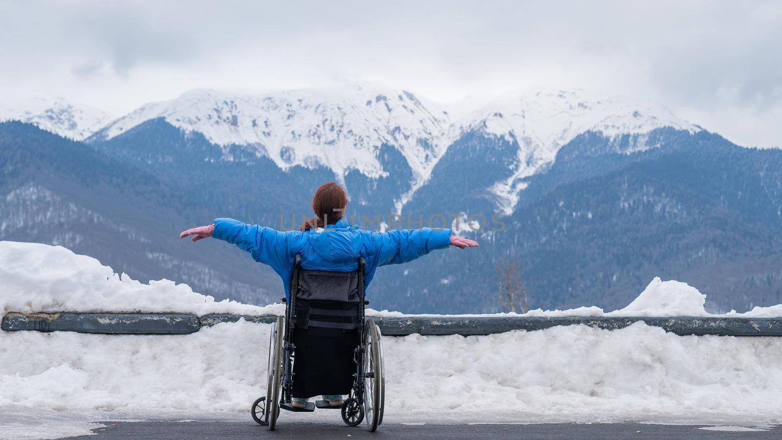 Rear view of a woman in a wheelchair spread her arms to the side like wings in the mountains in winter