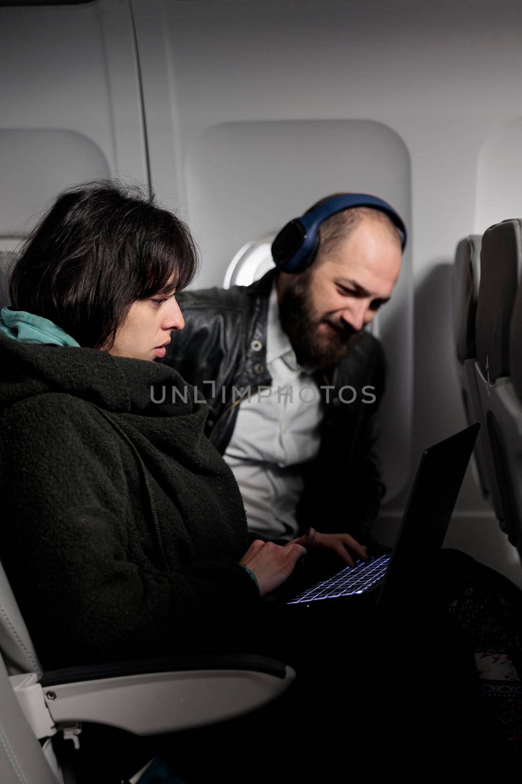 Couple travelling on holiday trip with aerial transportation, using laptop with online internet on commercial flight. Man and woman browsing computer on holiday destination, flying with plane.