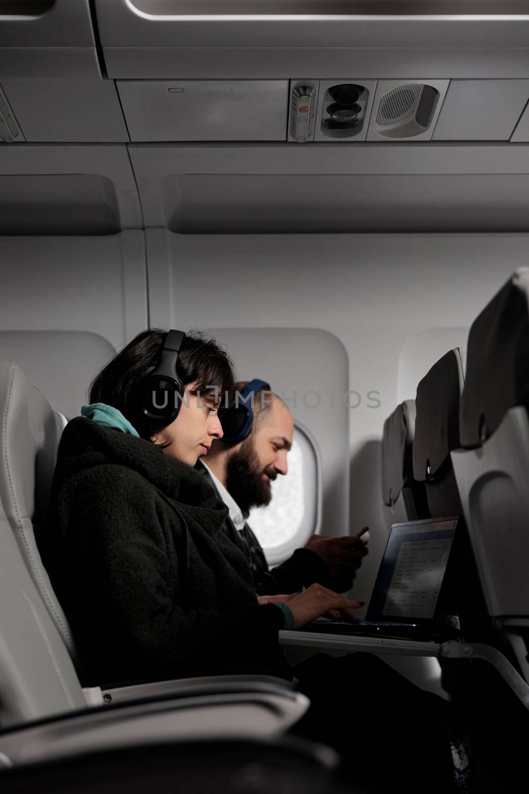 Man and woman using laptop and smartphone on airplane flight, waiting to arrive at holiday vacation. Couple of passengers working on devices and travelling with international airline.