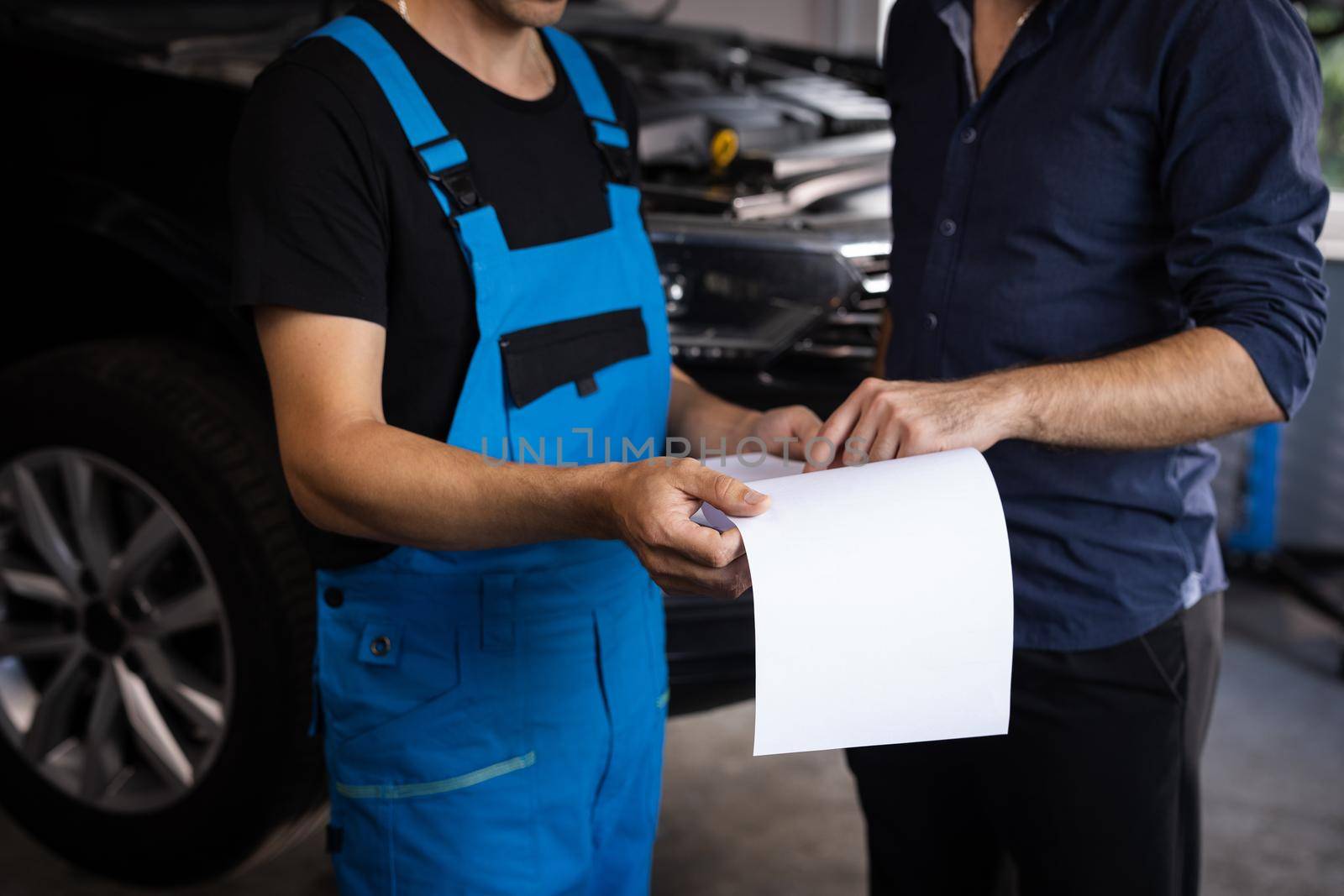 Mechanic and car owner signing paper at workshop. Customer and mechanic discuss upcoming car repair. Auto service, repair, deal and people concept by uflypro