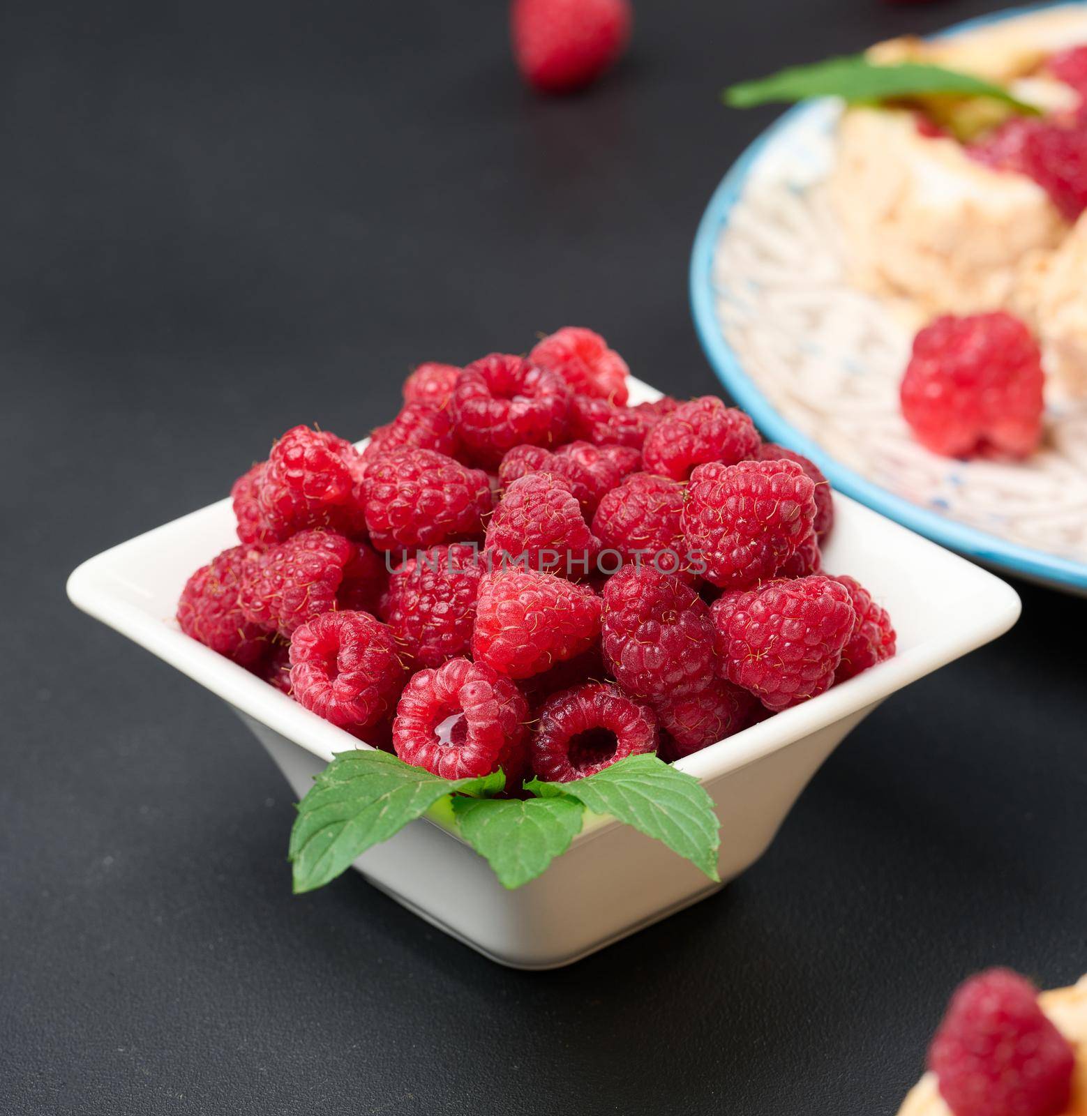 Ripe red raspberries in a white ceramic bowl on a black table