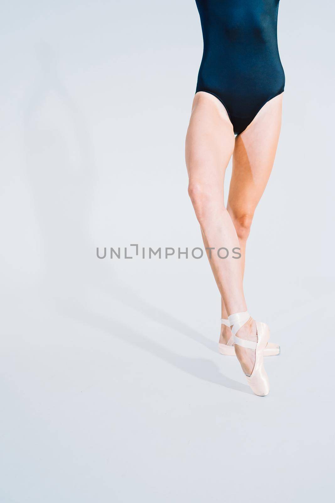 Close up of ballet dancer's legs in pointe. Woman practices exercises on white studio background. Ballerina's feet in shoes. Girl shows classic ballet pas. by kristina_kokhanova
