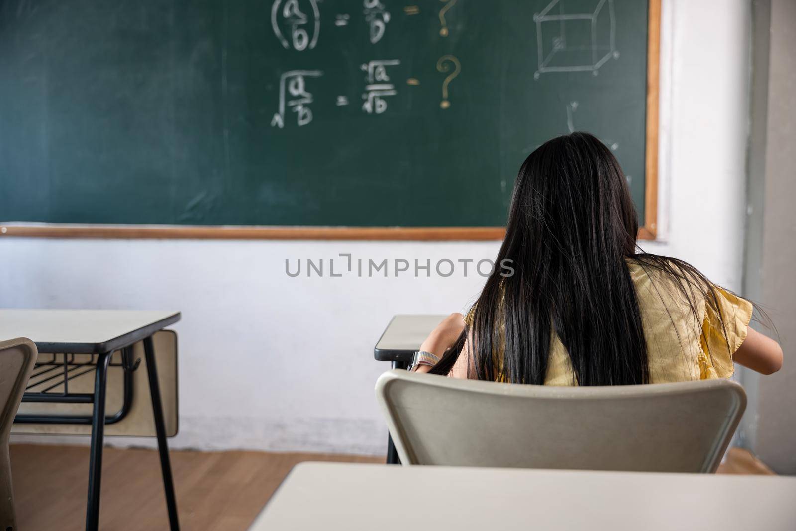 Education. Back view of school girl on lesson in classroom write hardworking on blackboard, primary child is sitting lessons at table in school writing or drawing in notebook, Back to school concept