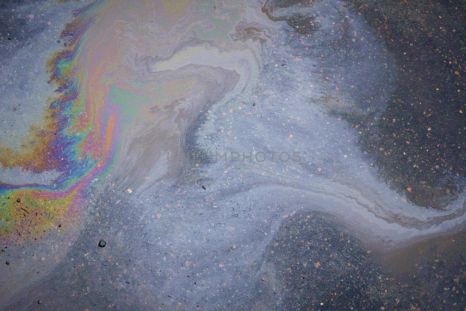 Oil stain on the asphalt, rainbow-shaped colored gasoline stains on an asphalt road as a texture or background