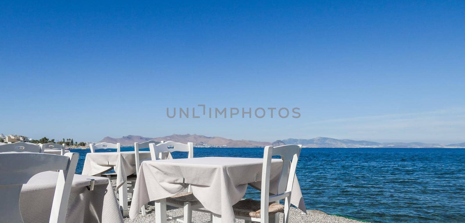 White restaurant tables on the beach in summer - travel, vacation and summer concept. The perfect lunch with a sea view