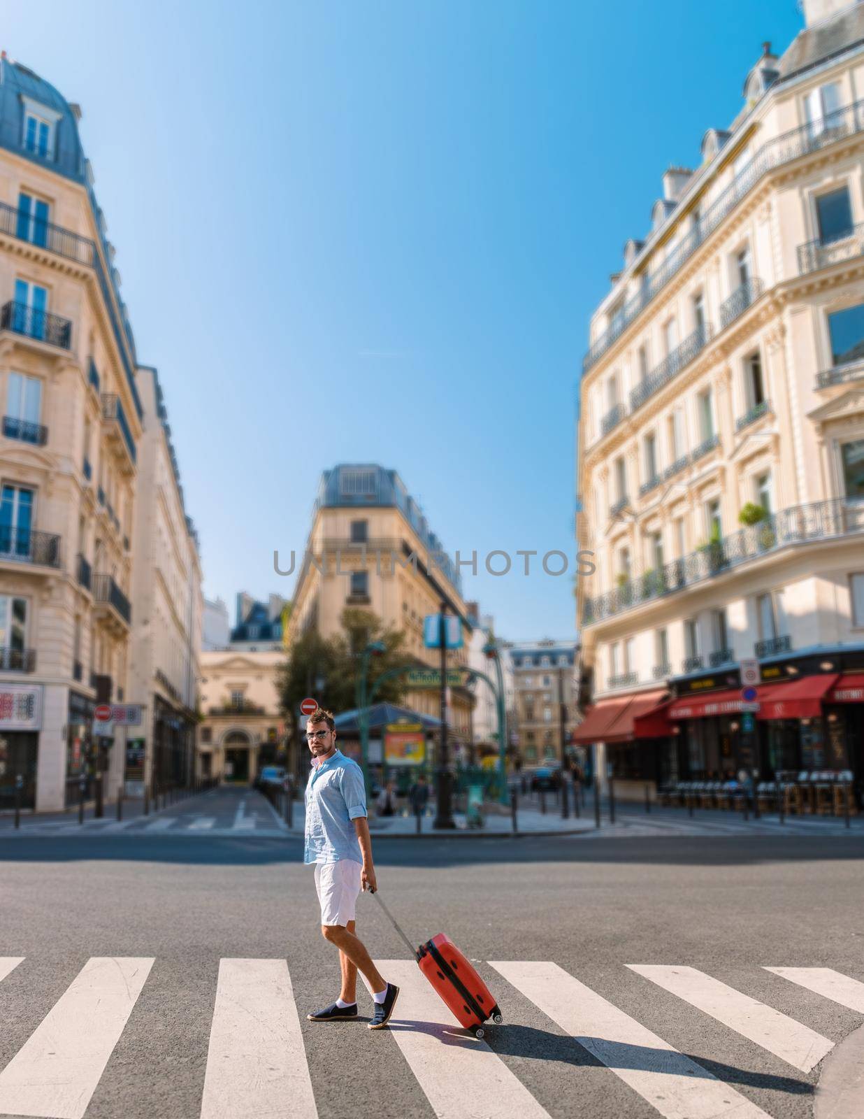 Young men on a city trip in Paris, a man traveling with trolley luggage. Man walking on the street with a small travel trolley