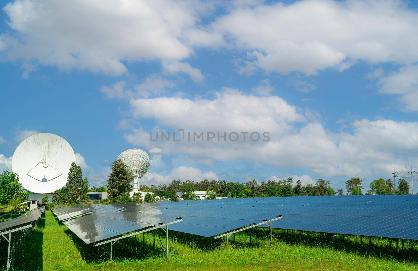 Solar farm and green field with blue sky. Big satellite dish near solar farm. Solar power for green energy. Photovoltaic power plants generate solar energy. Renewable energy. Sun power for commercial. by Fahroni