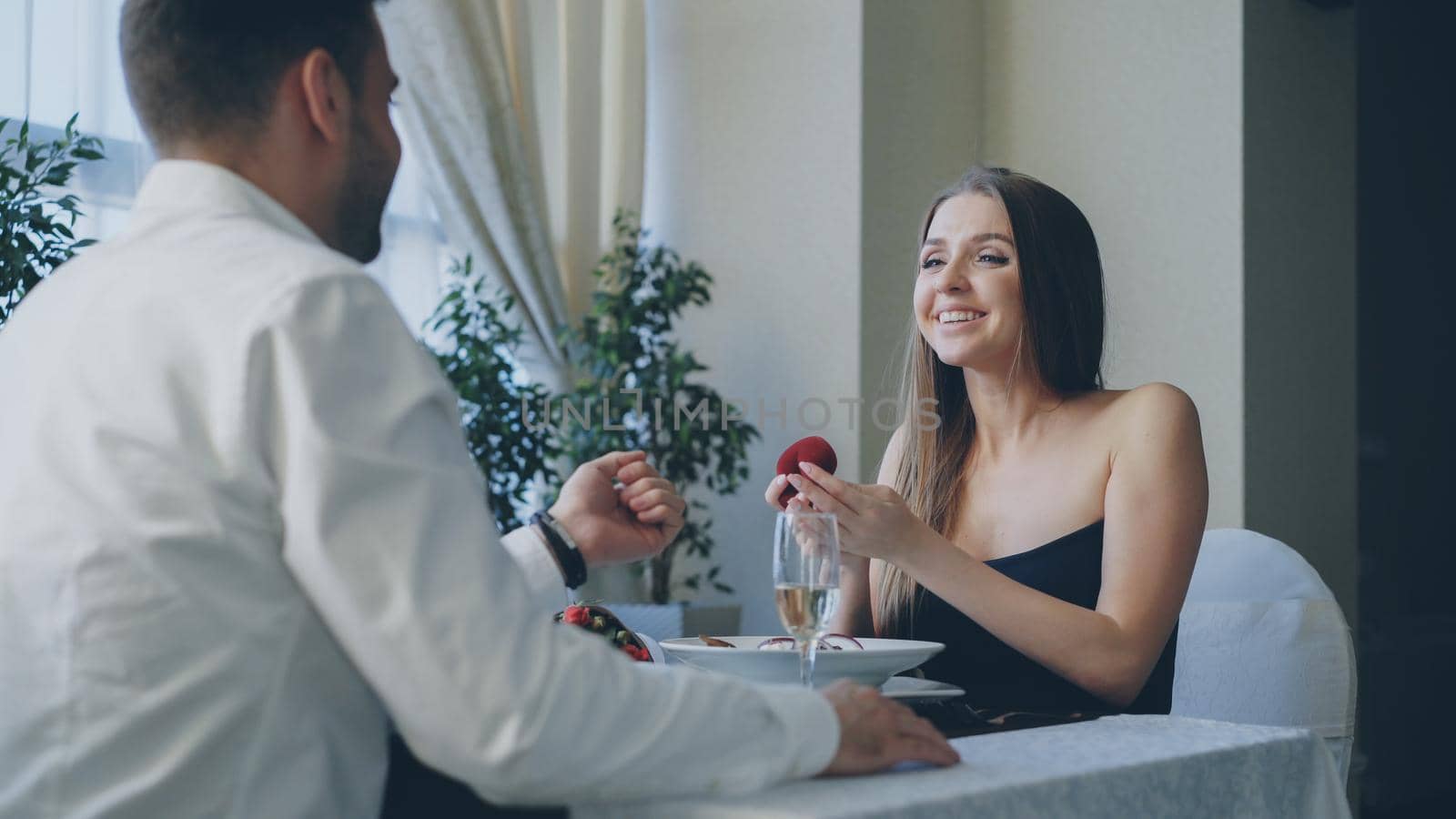 Beautiful young woman is happy and surprised after getting marriage proposal from her boyfriend in restaurant by silverkblack