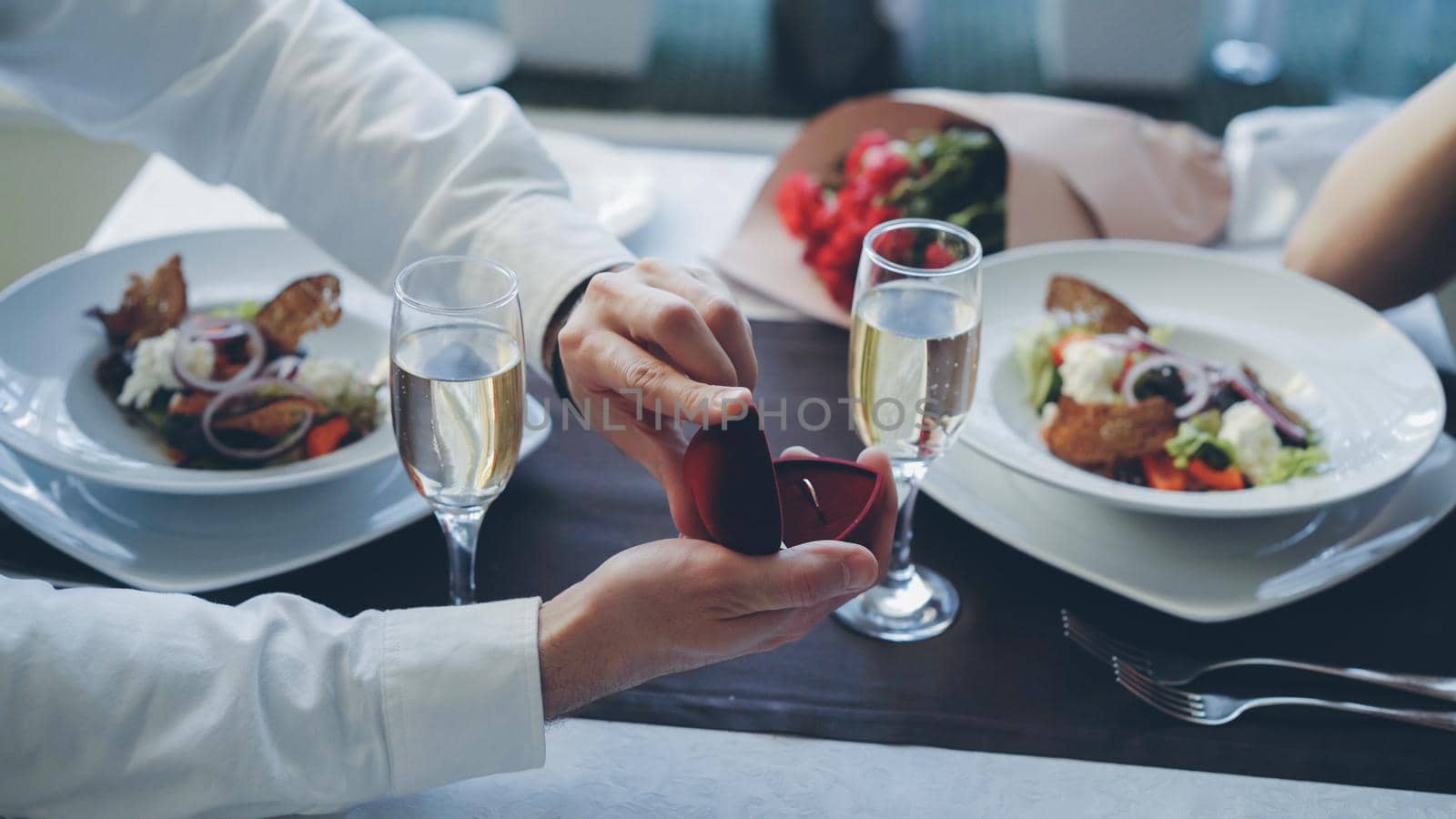 Close-up shot of beautiful ring being placed on female finger during marriage proposal at romantic dinner in restaurant. Engagement and fine dining concept. by silverkblack