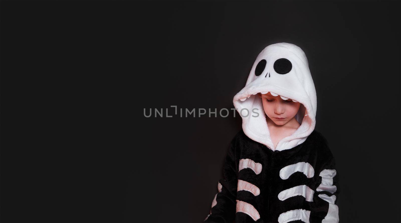 Halloween. Little cheerful boy in a plush skeleton costume. The child laughs and is happy. Banner on black background with copy space for text. Halloween holiday concept