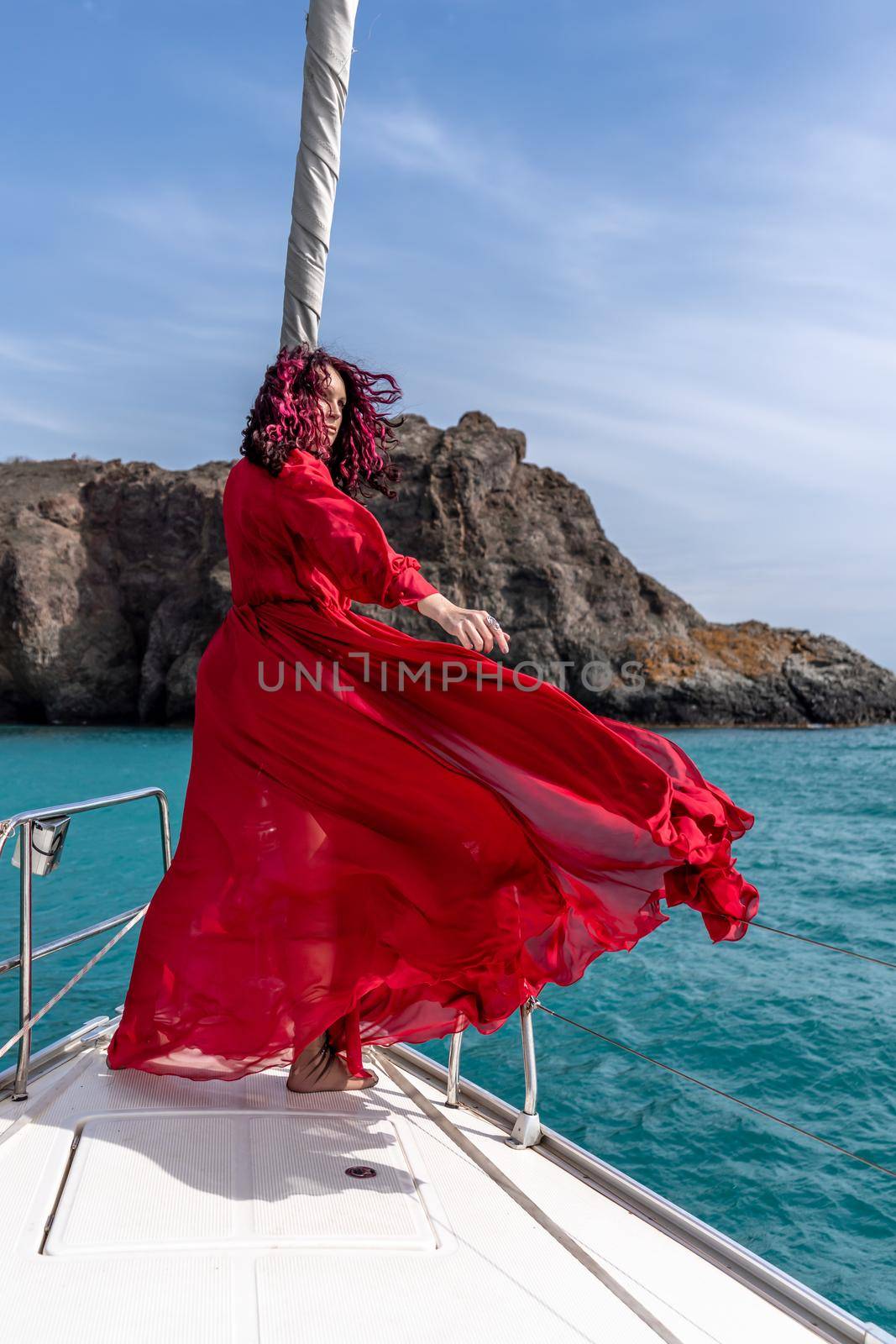 Attractive middle-aged woman in a red dress on a yacht on a summer day. Luxury summer adventure, outdoor activities. by Matiunina