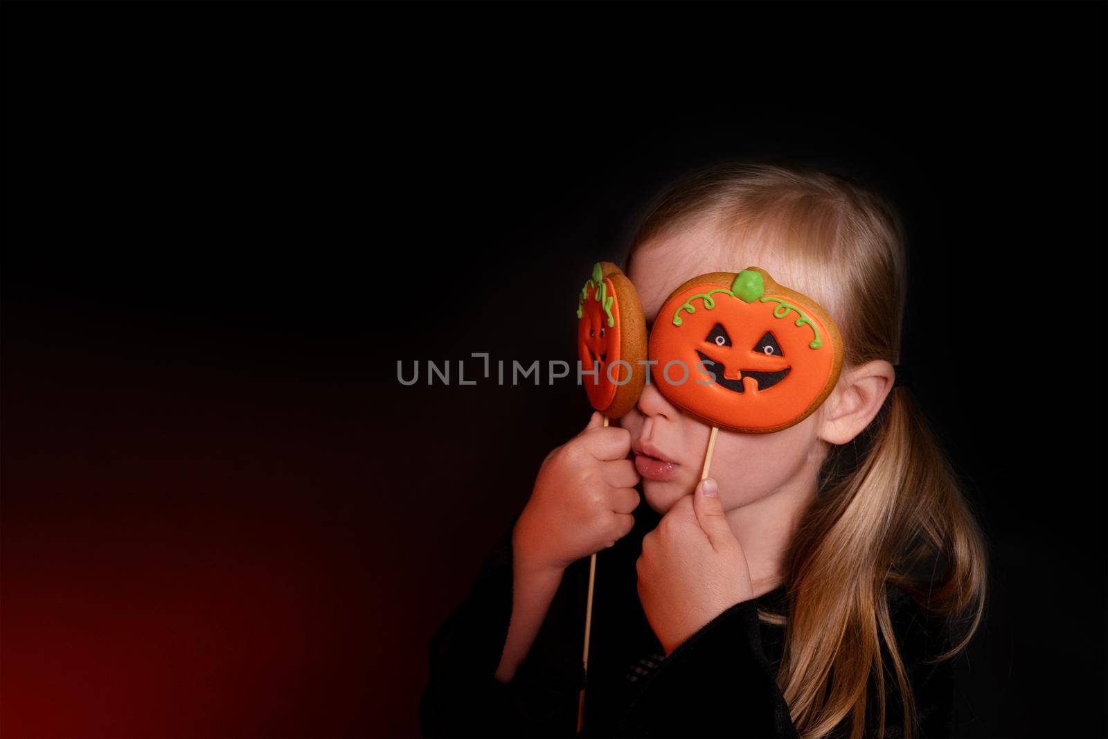 Portrait of a girl on a black background with gingerbread cookies for Halloween by Ramanouskaya