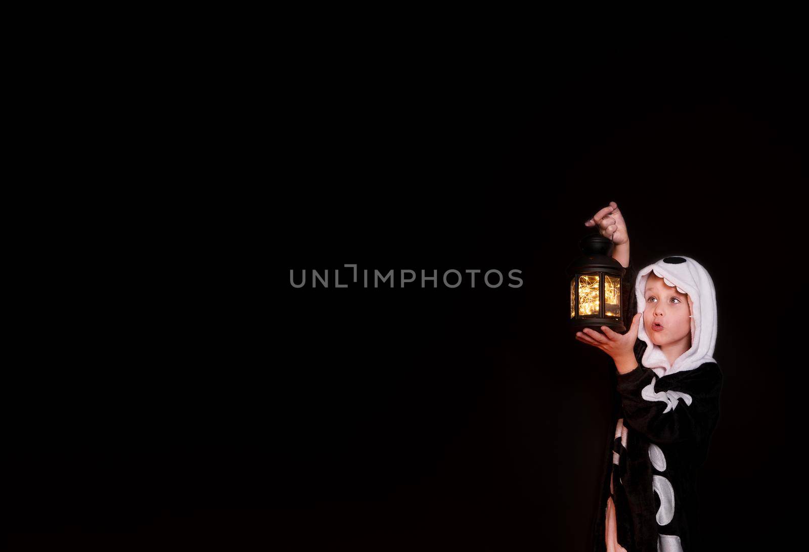 Halloween. A small, cheerful boy in skeleton costume holds pumpkin lantern in his hands. The child is laughing and happy. Banner on black background with copy space for text. Halloween holiday concept