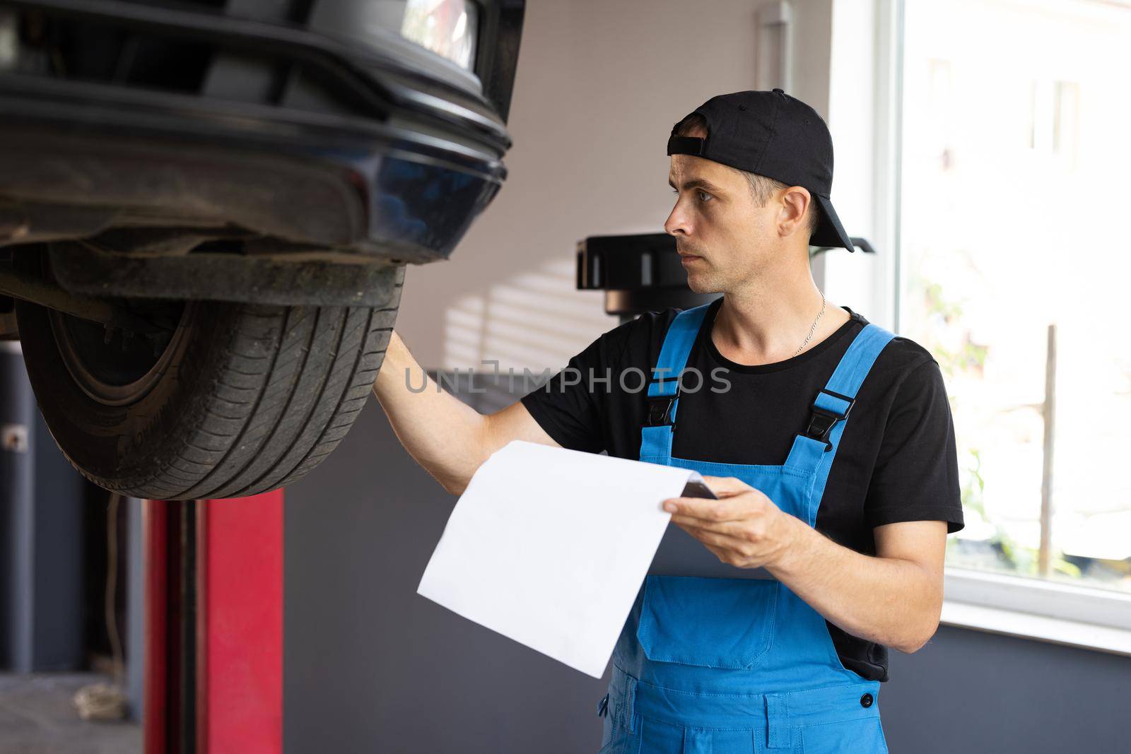 Car service employe inspect car. Mechanic inspects the car undercarriage way and makes a note on his inspection sheet. Automobile service, car mechanic. Modern workshop