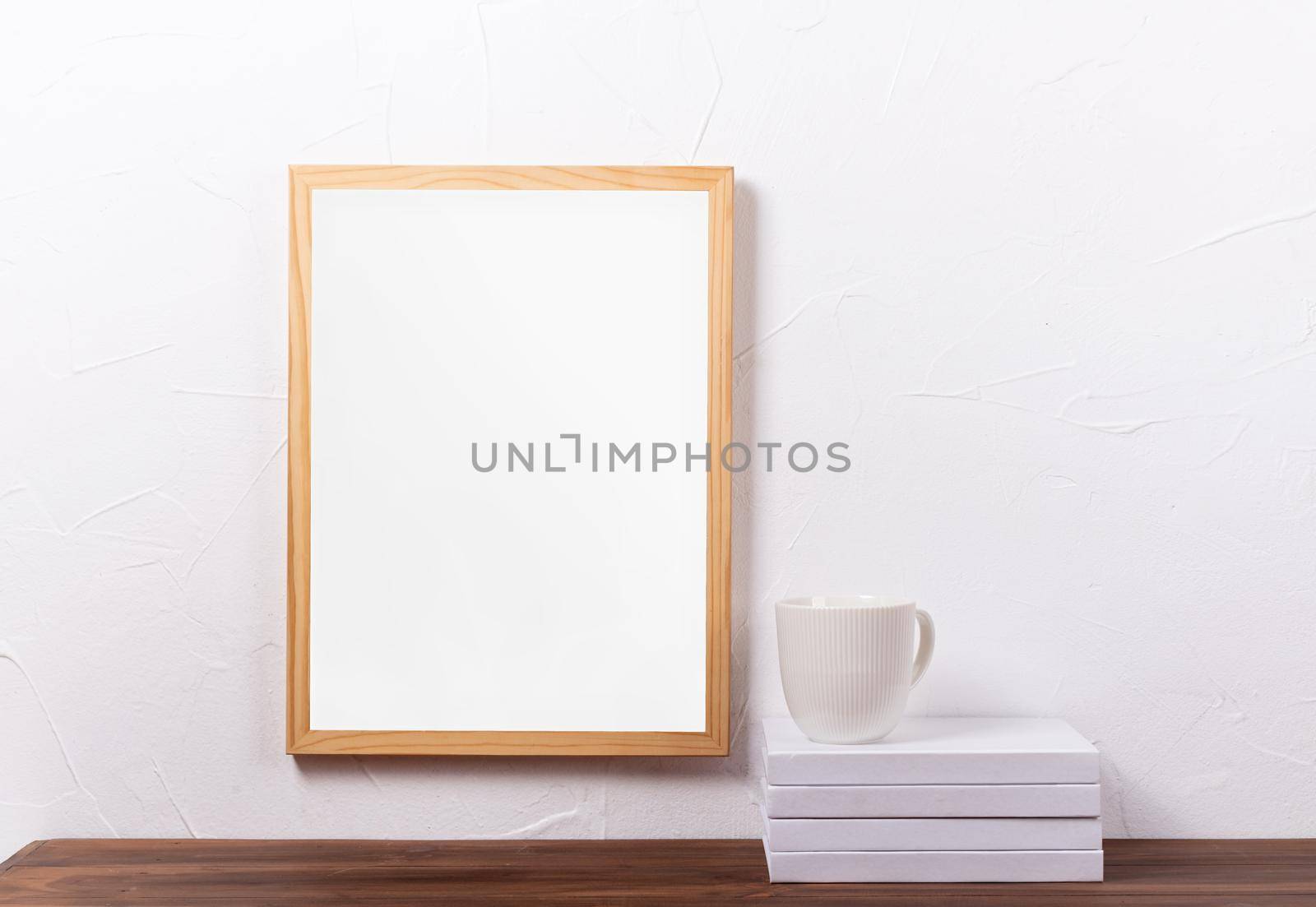 White frame mockup hanging on the wall with stack of books and coffee cup , mockup design
