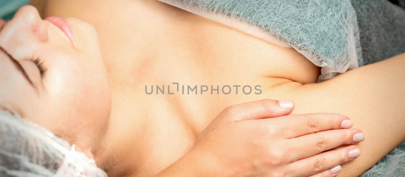 Side view hands of female therapist making massage of shoulders to young caucasian woman in spa beauty salon