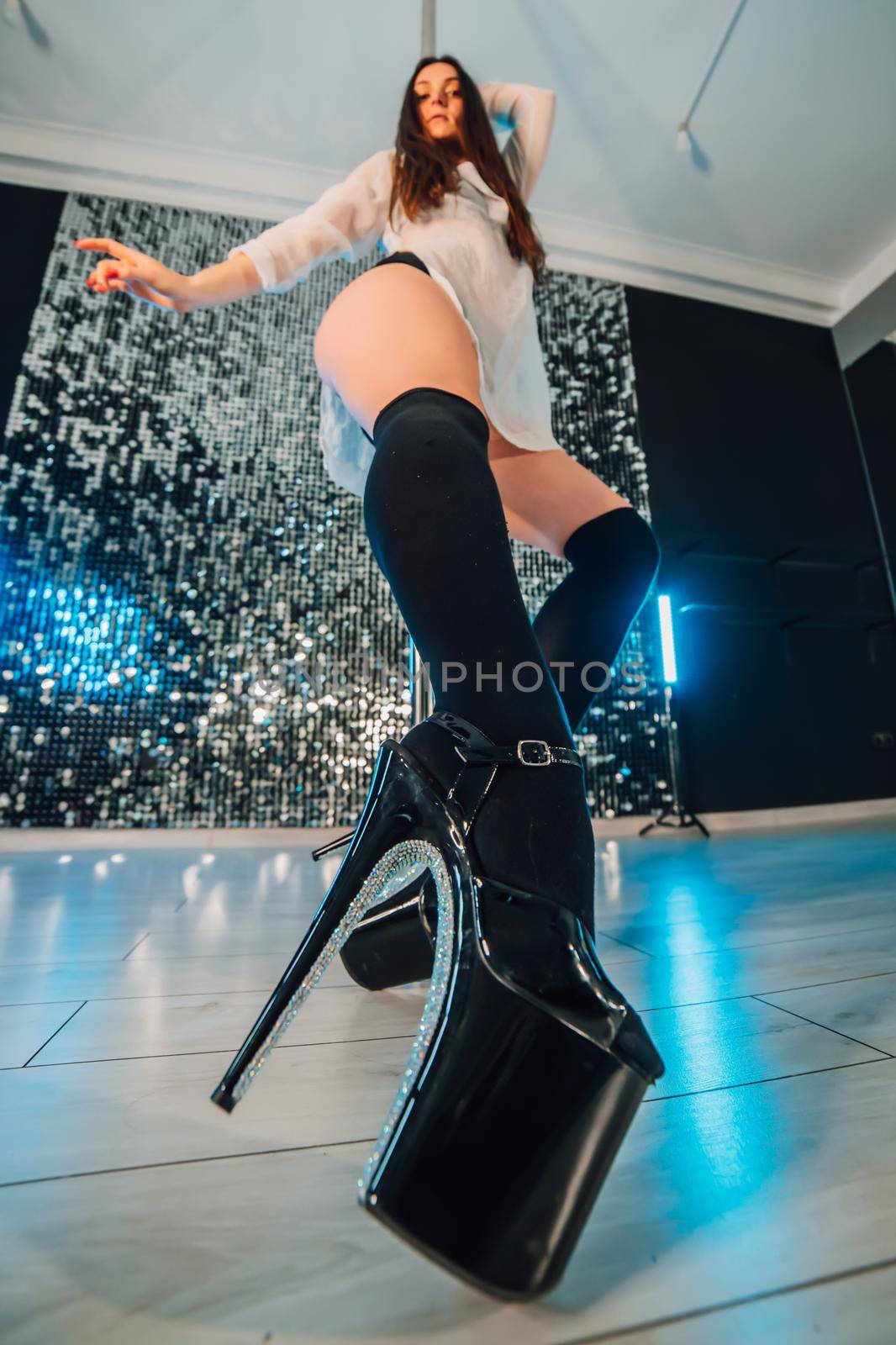 Alluring woman with long hair posing with pylon on shining wall background. Pole-dance, sexy, temptation concept. High quality photo