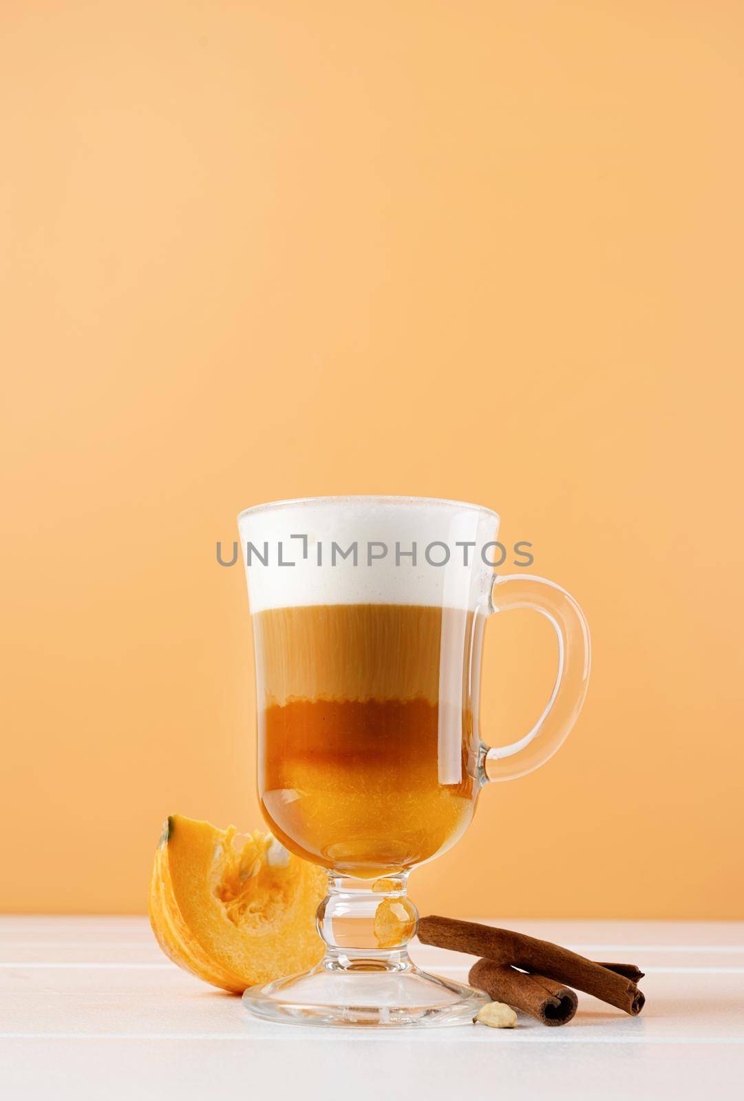 Autumn hot drinks. Pumpkin spice latte in a glass mug with cinnamon on orange background with copy space