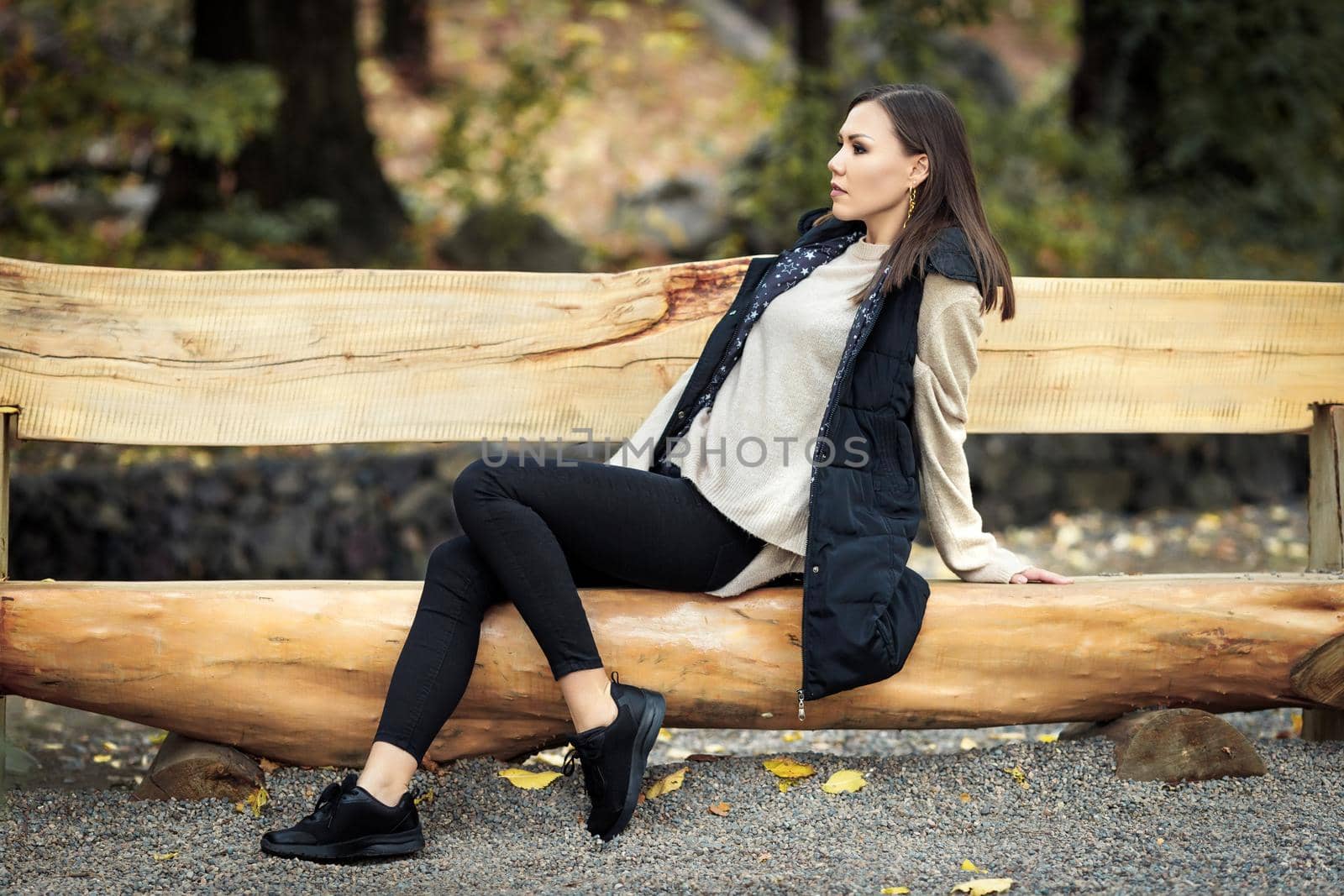 Profile of a young woman in full growth sitting on a wooden bench in a park outdoors. High quality photo