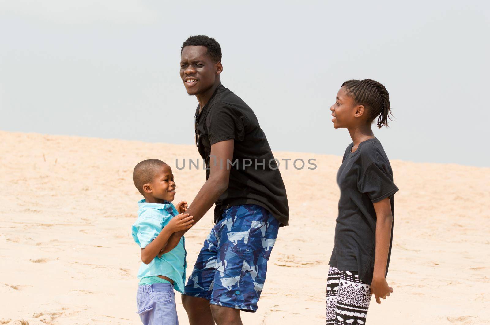 young man wanting to lift his little brother and little sister looks at them smiling.