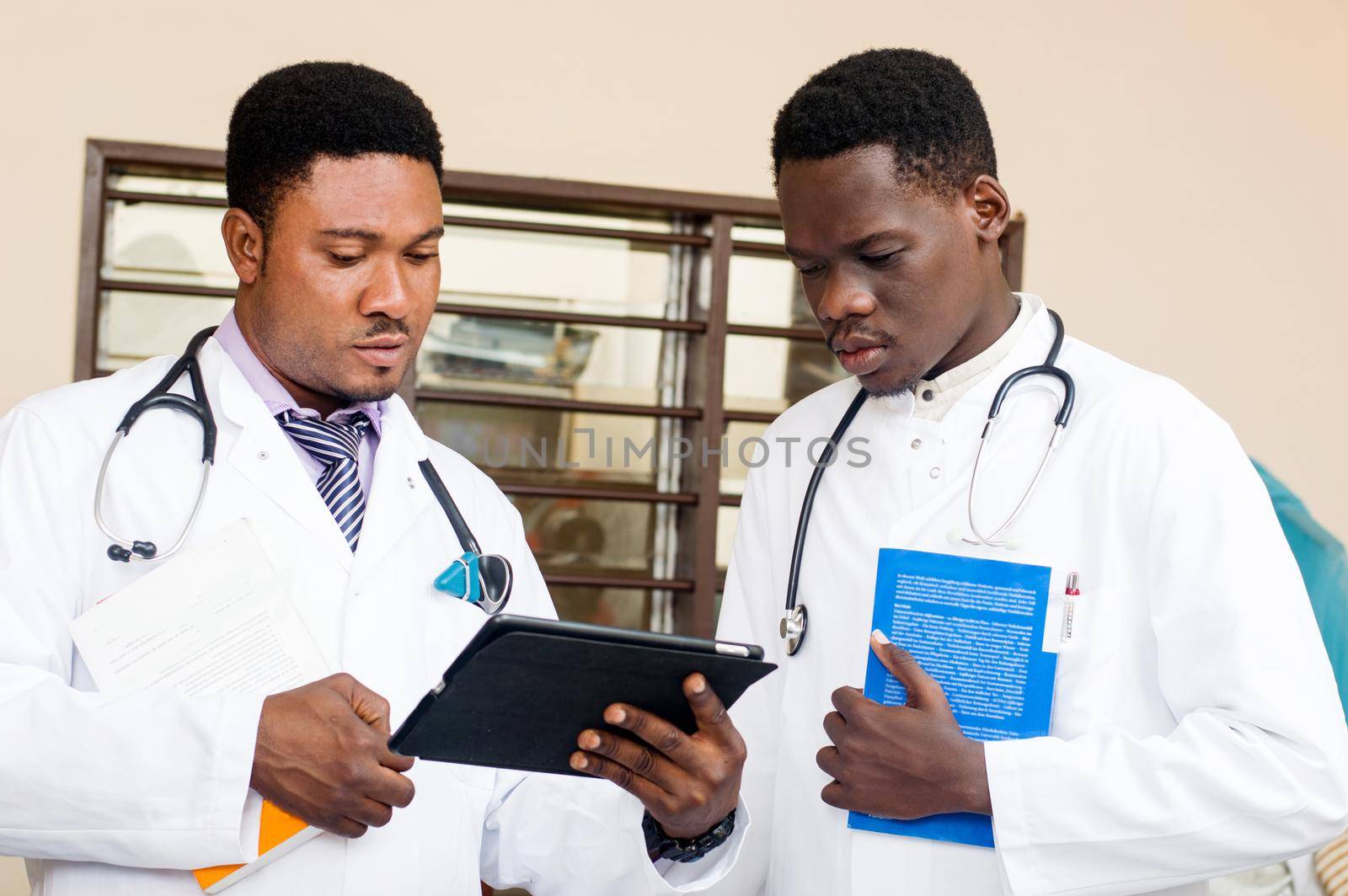 two standing doctors share a digital tablet in the office. by vystek