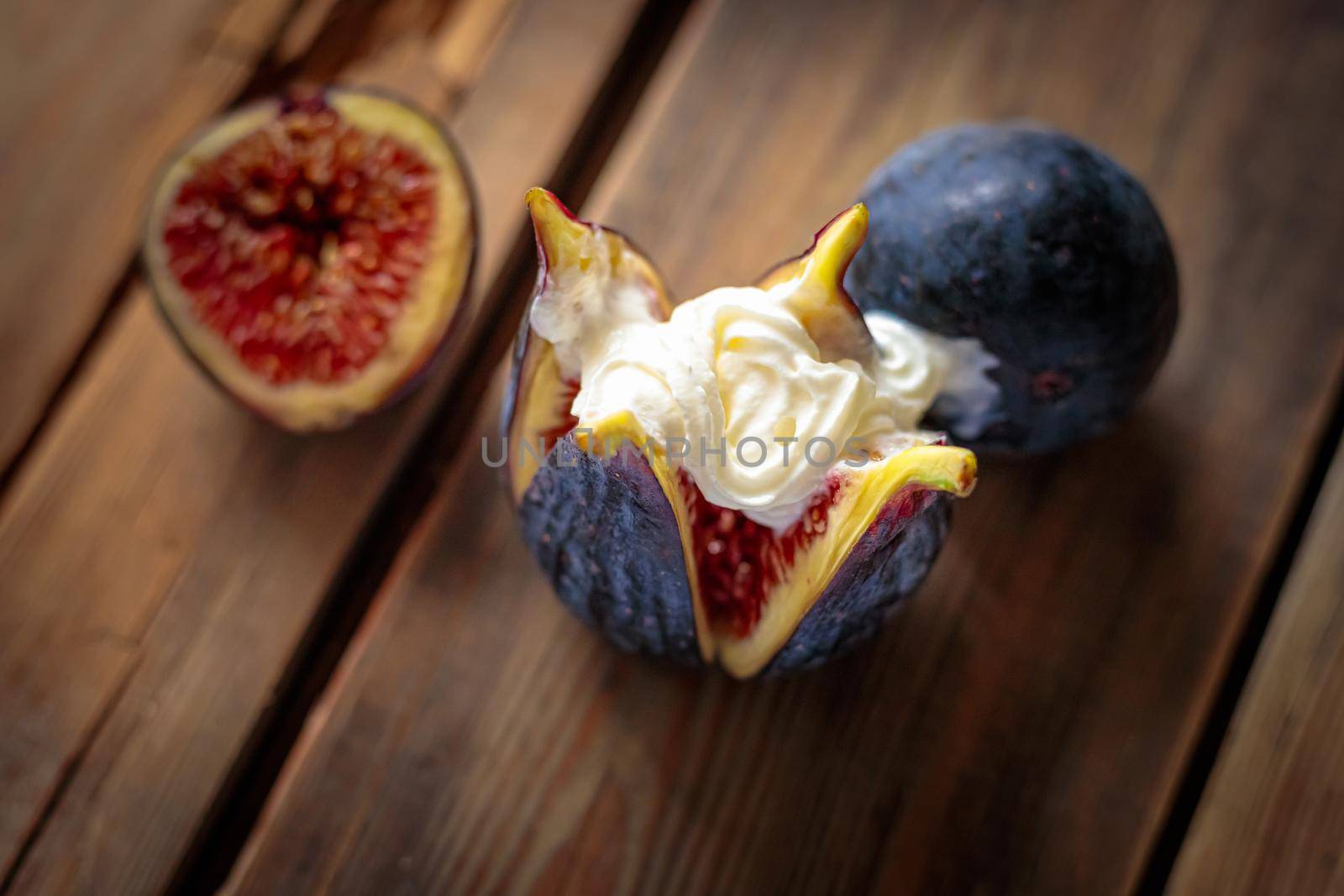 Fresh sliced purple figs with whipped cream on a wooden background from old boards. Raw exotic figs. Low key