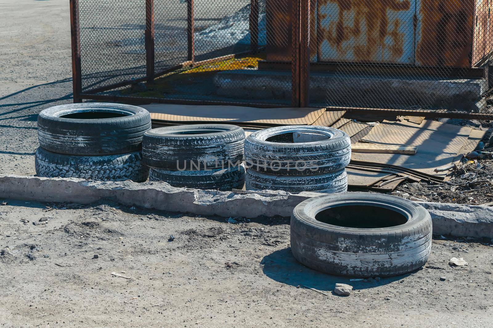A pile of used car tires lies on the sand in an old dump near the road