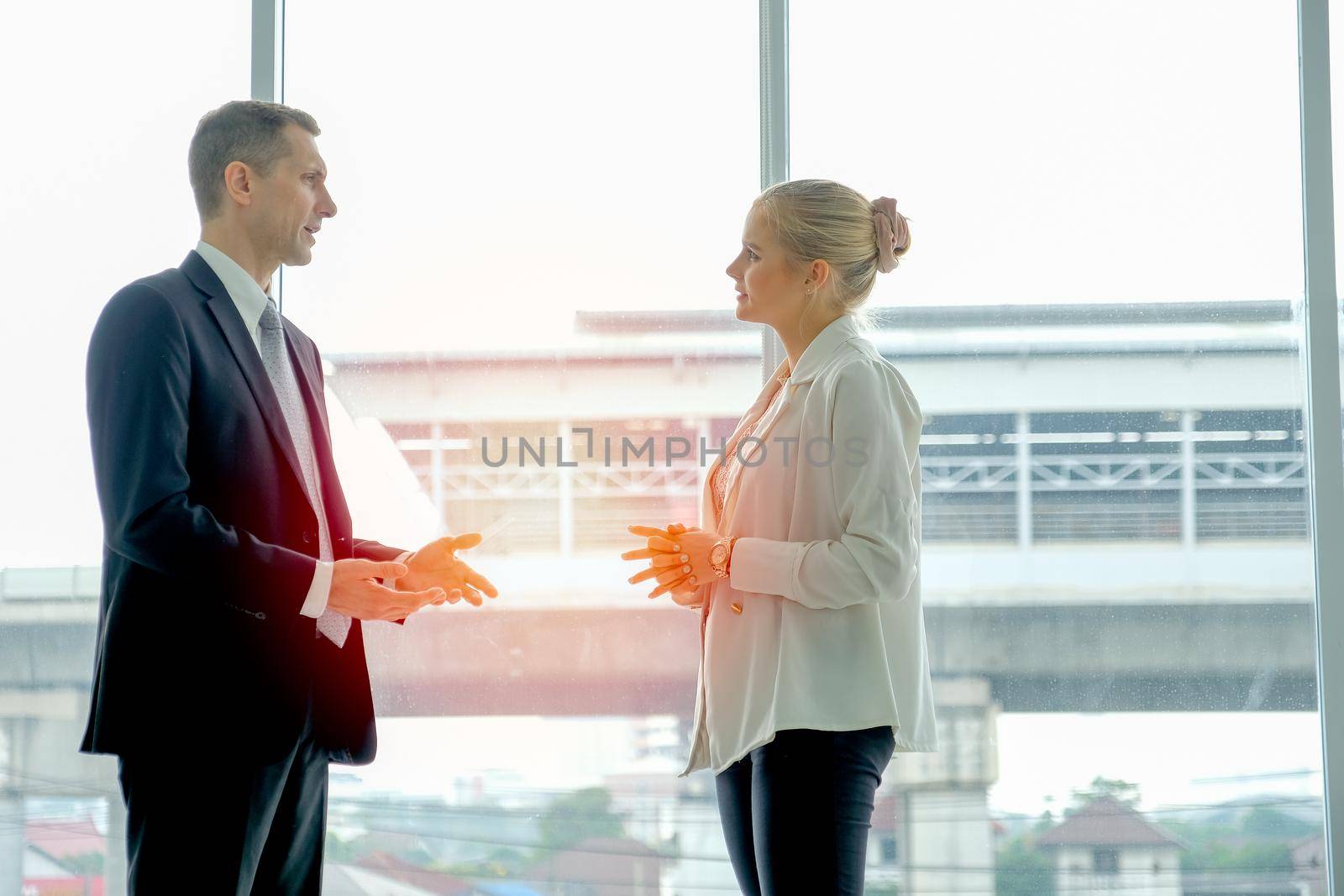 Business man stands and discuss with young beautiful woman in the room with glass windows.