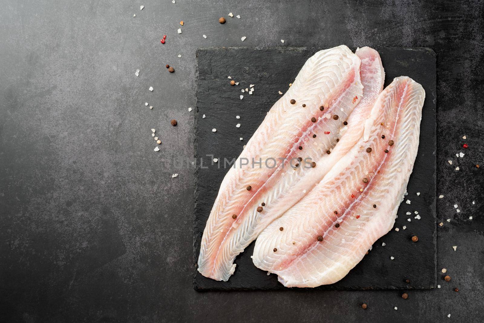 Fresh raw white fish fillet Pangasius with spices and lemon on state plate on a stone background with copy space for your text