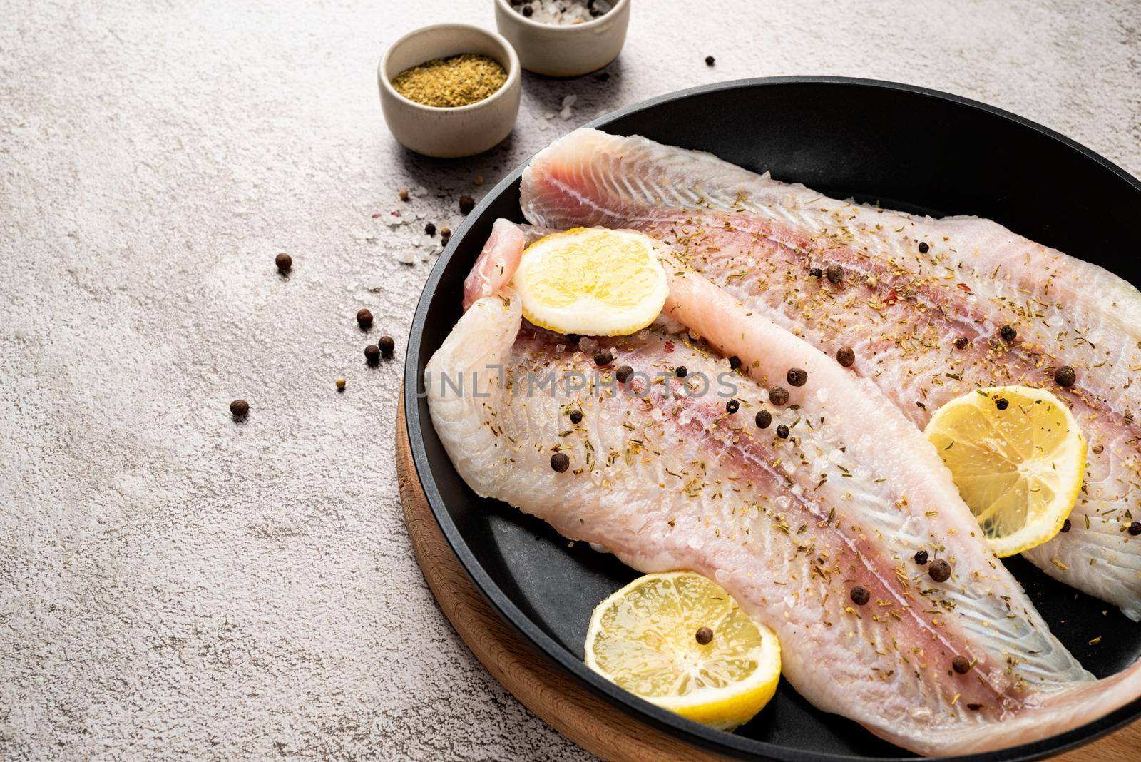 Fresh raw white fish fillet Pangasius with spices and lemon in frying pan on a stone background with copy space for your text