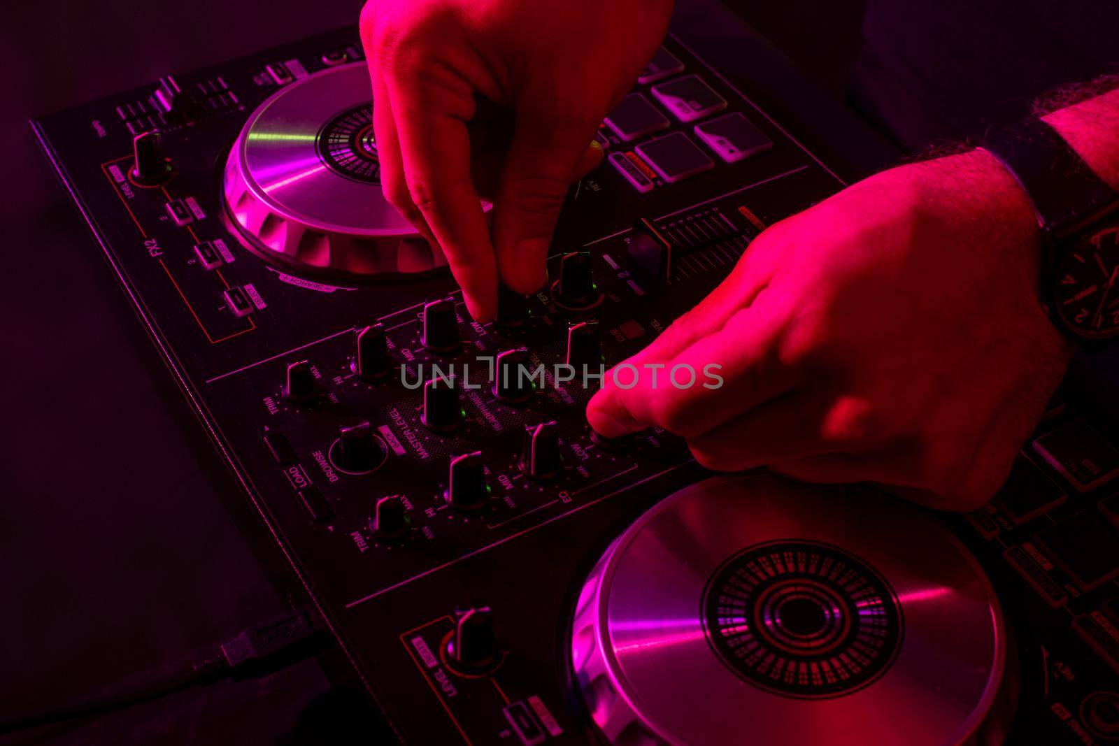 Dj mixing on turntables with color light effects. Soft focus on hand. Close-up. Fun, youth, entertainment and fest concept