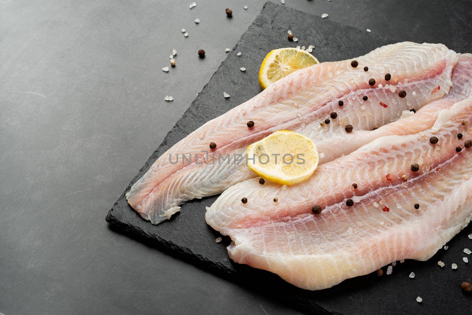 Fresh raw white fish fillet Pangasius with spices and lemon on state plate on a stone background with copy space for your text