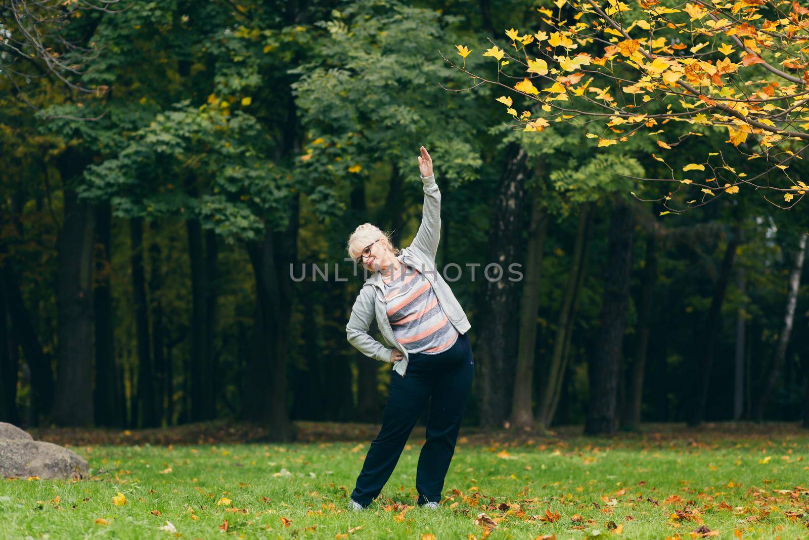 Senior woman standing and doing sports in the park on the grass, exercising, leading a healthy active lifestyle