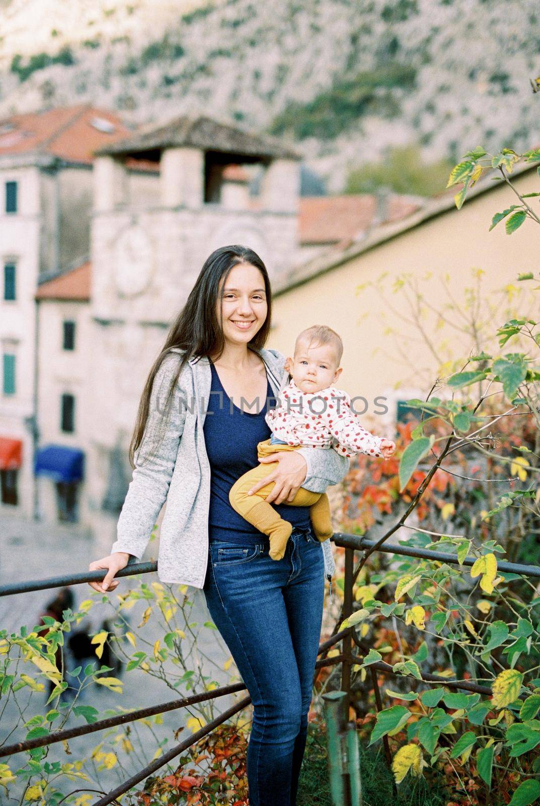 Mom with a baby in her arms stands on the balcony against the backdrop of old houses. High quality photo
