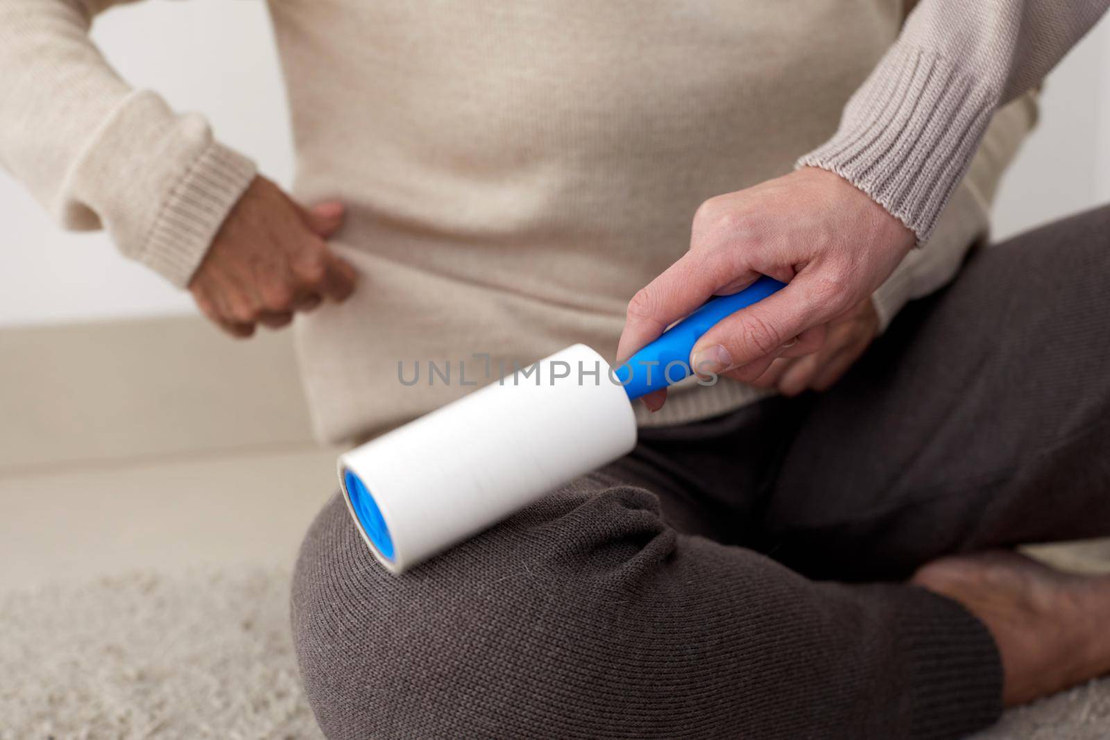Crop unrecognizable person helping woman and cleaning her clothes with lint roller at home