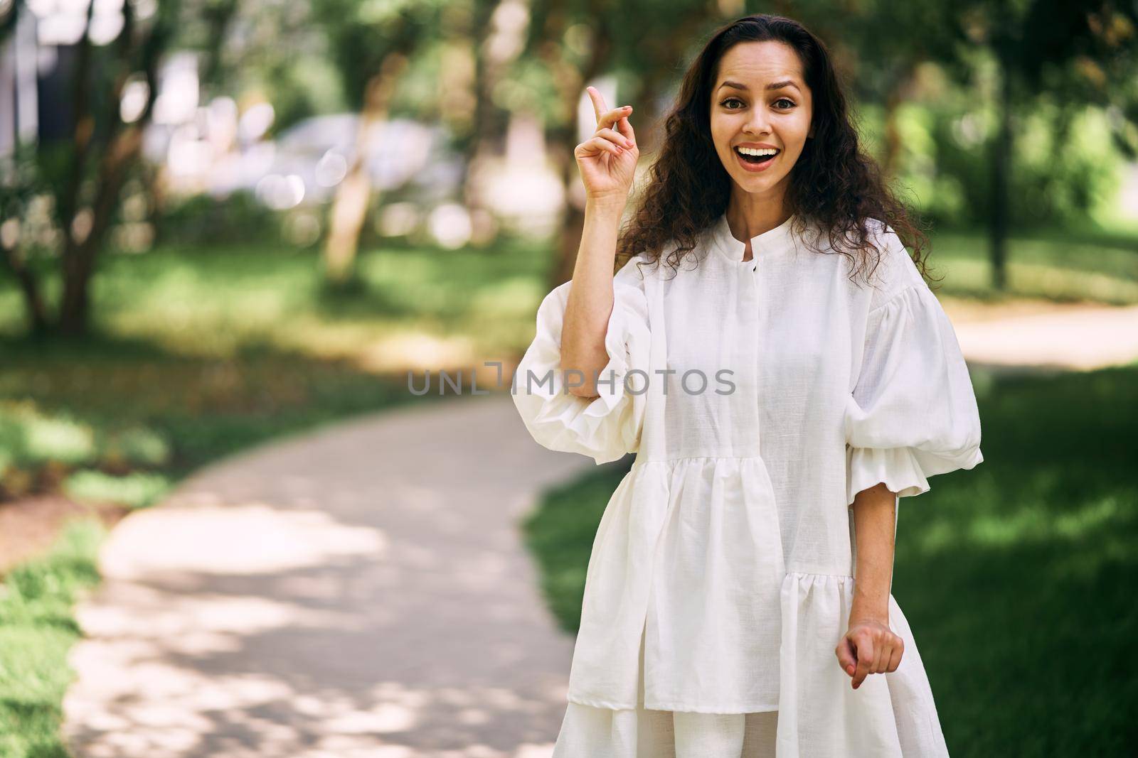 Cheerful curly-haired brunette girl with open mouth raises her index finger. Girl has an idea. High quality photo