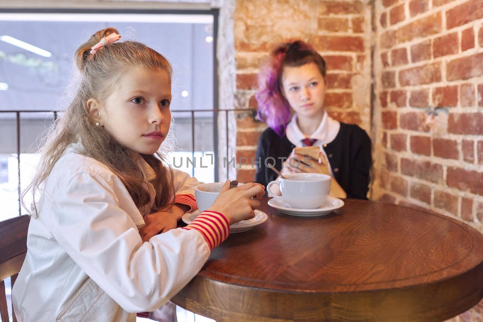 Children, two sisters sitting together in cafe at table by VH-studio