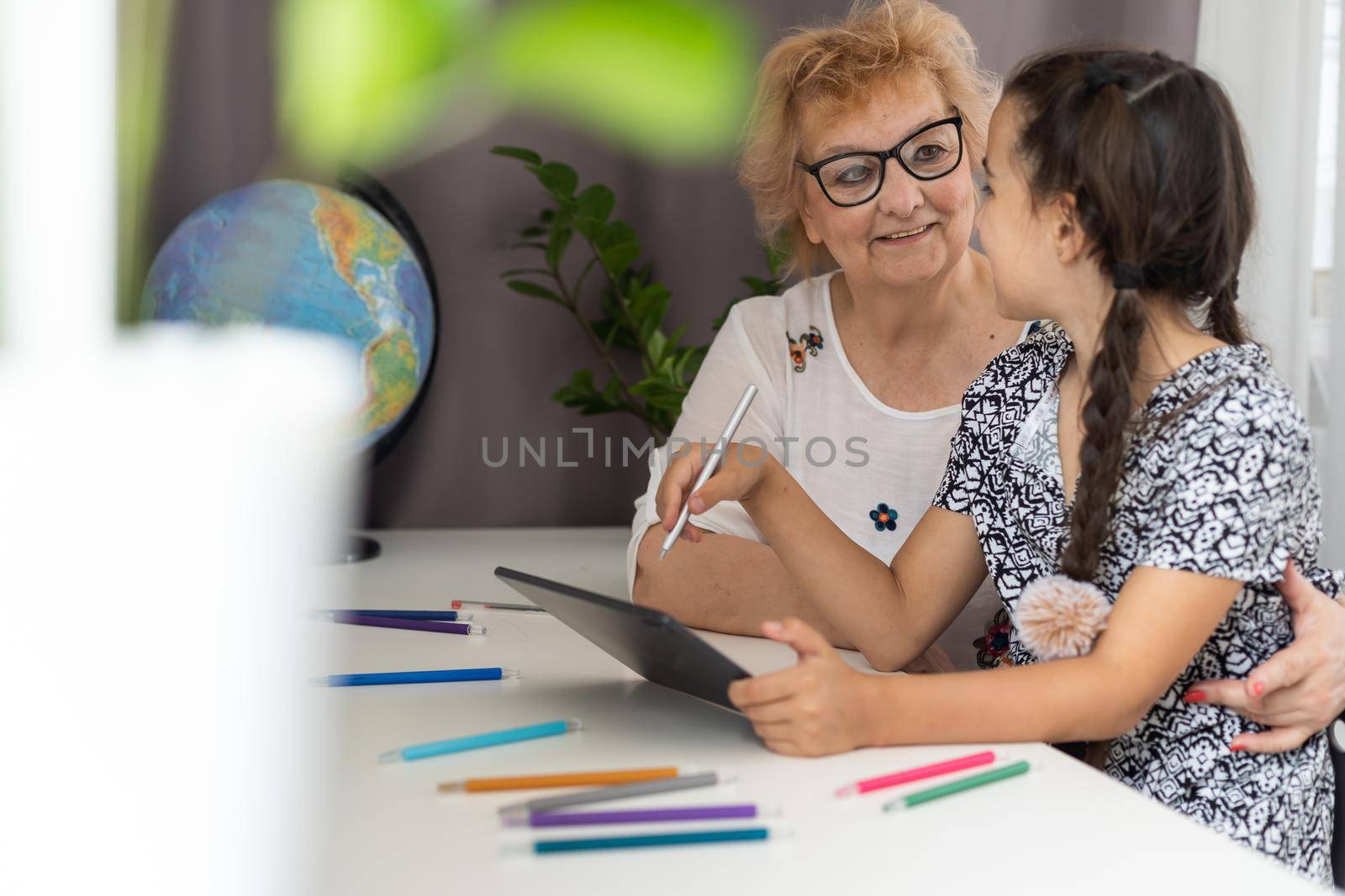 Cute little girl with her grandmother looking at tablet at home by Andelov13