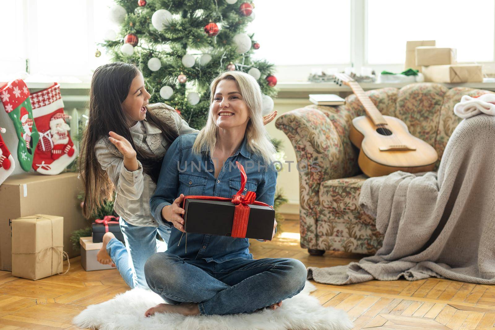 Merry Christmas and Happy Holidays. Cheerful mother and her cute daughter girl exchanging gifts. Mom and little child having fun near tree indoors. Loving family with presents in room by Andelov13