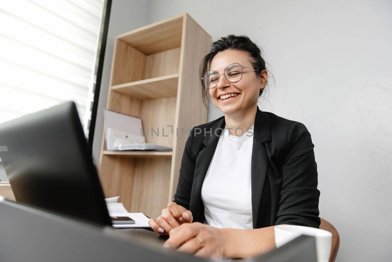 The girl in the office leads an online conference smiling and working at her laptop. Work in the office, girl office manager