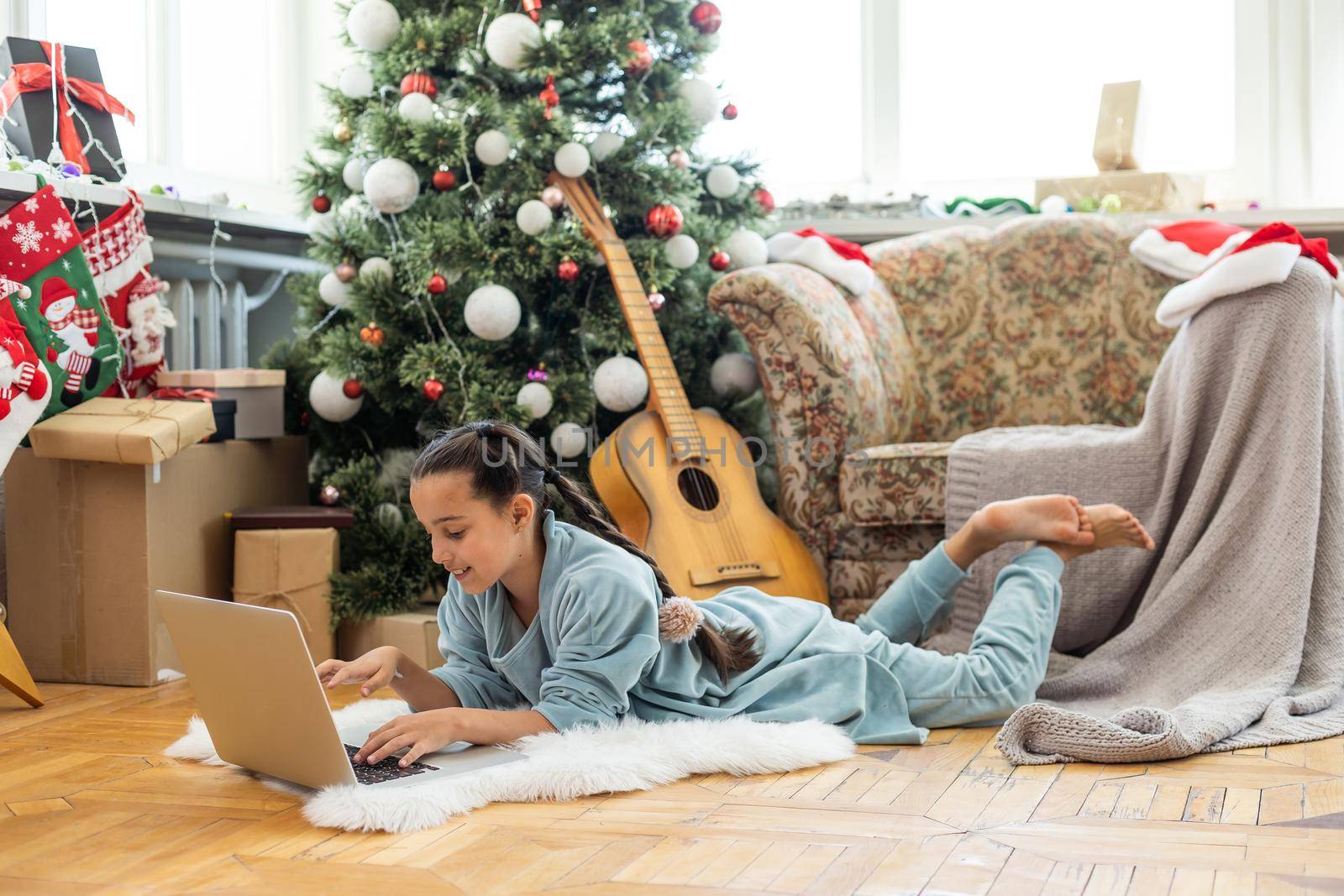 winter holidays, technology and children concept - little student girl with laptop computer at home over christmas tree background