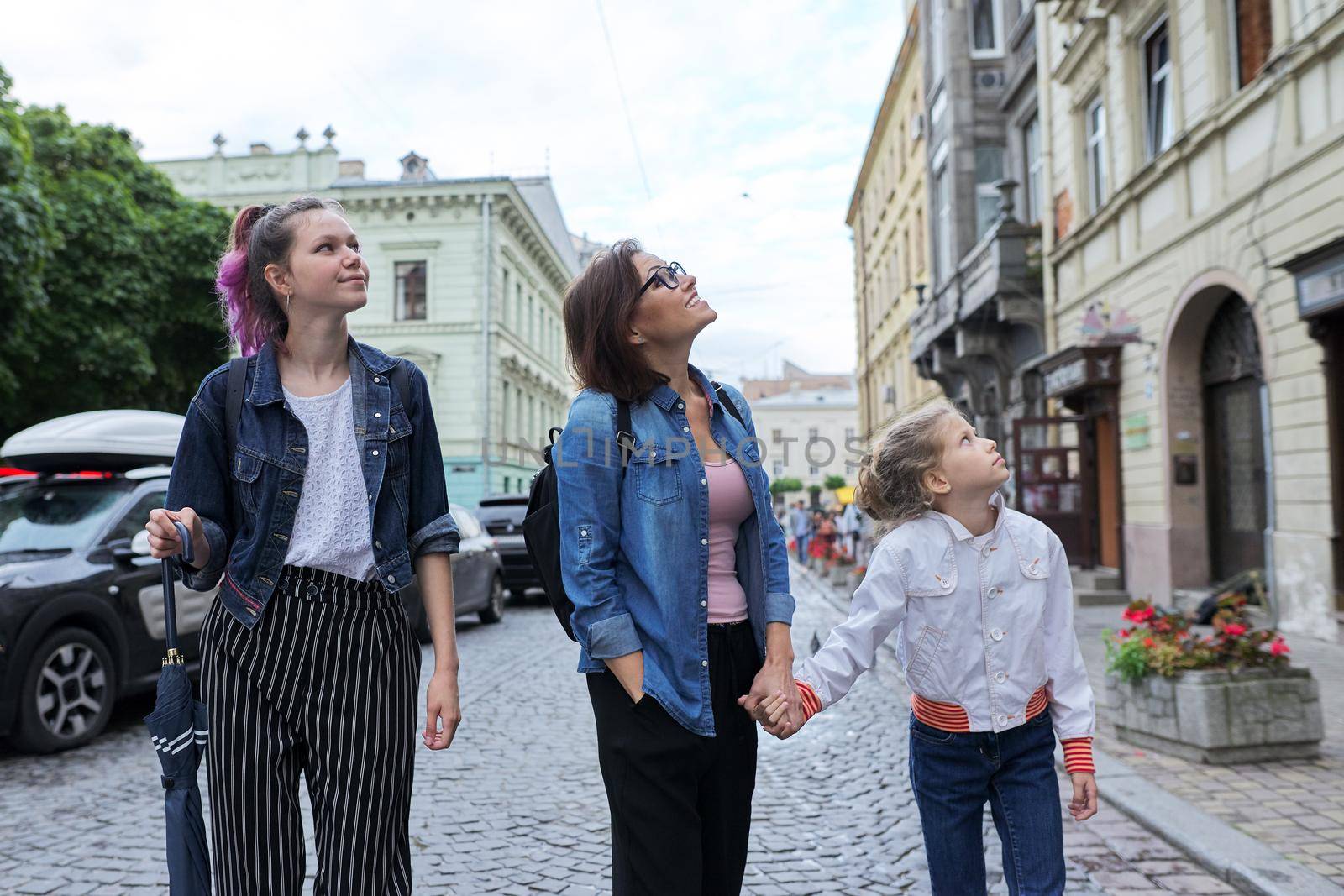 Mother and children daughters teenager and younger walking together on city street and looking up